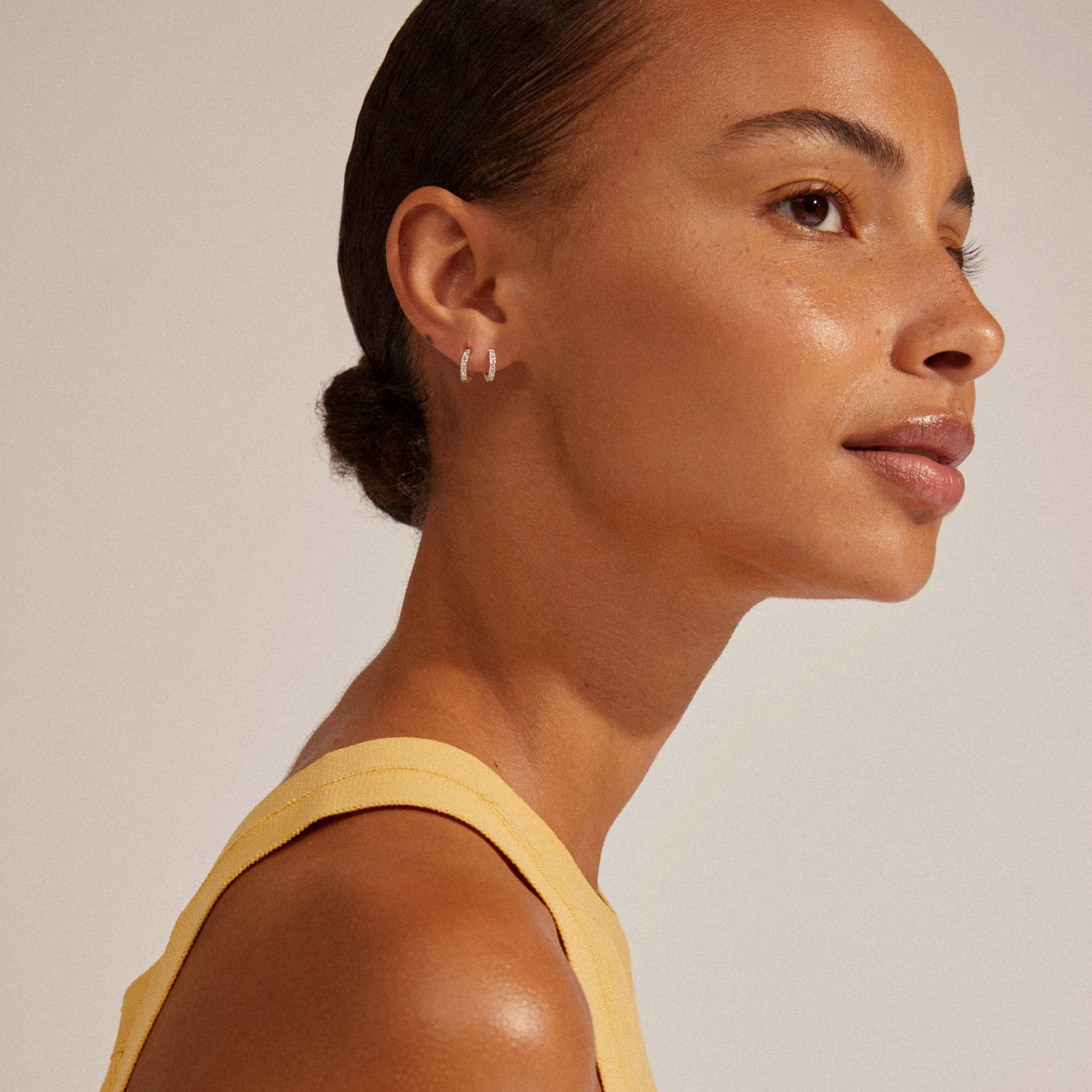 EBNA mini crystal huggie hoops silver-plated on a woman wearing a yellow tank top, showcasing the hoops' sparkling Preciosa crystals and smart click lock mechanism.