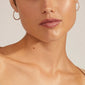 Close-up of a person wearing EBNA maxi crystal hoops, silver-plated earrings by Pilgrim, showcasing their smooth design and easy-to-use click lock.
