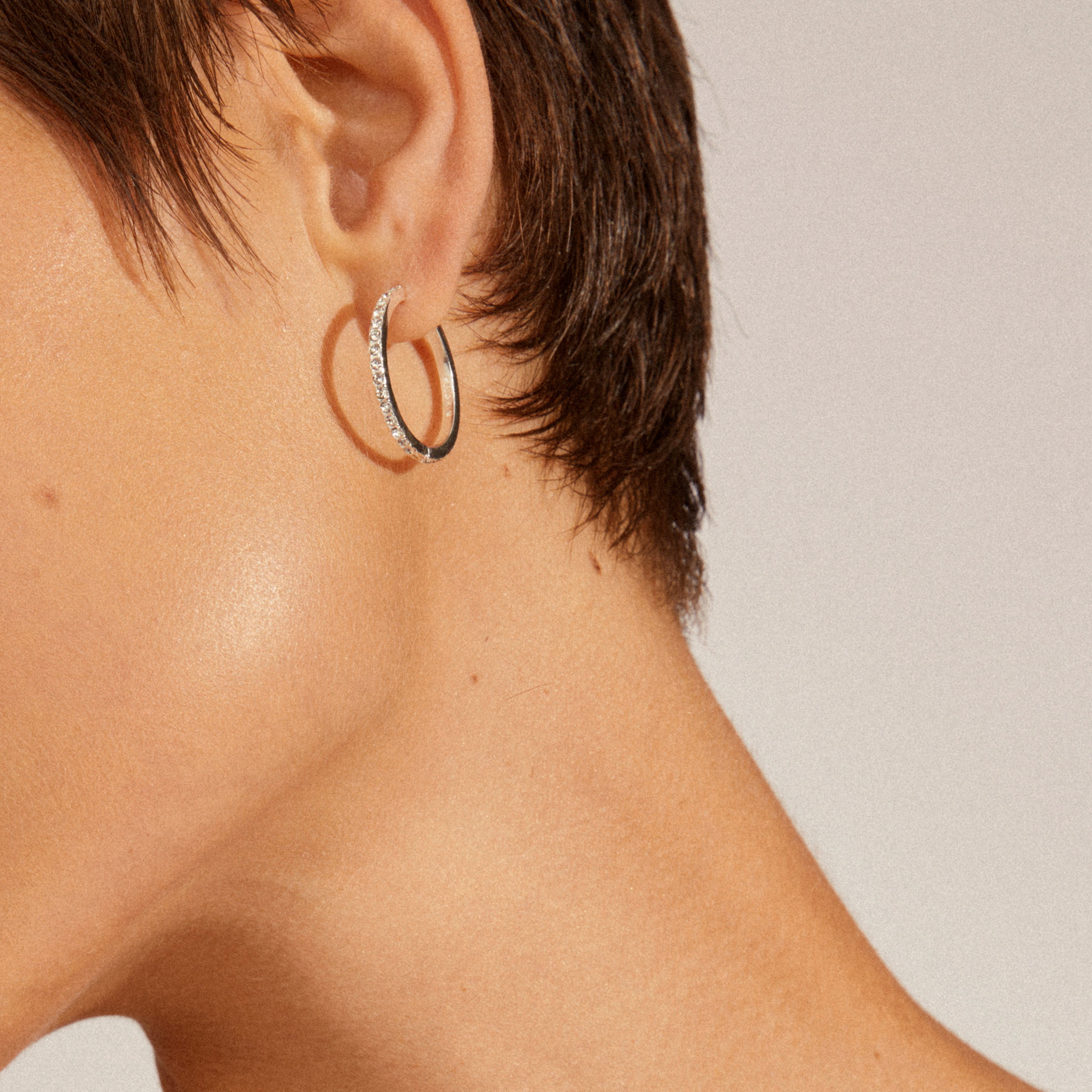Side view of a person wearing EBNA maxi crystal hoops silver-plated, featuring sparkling stones in a silver hoop with a smart click lock for easy wear.