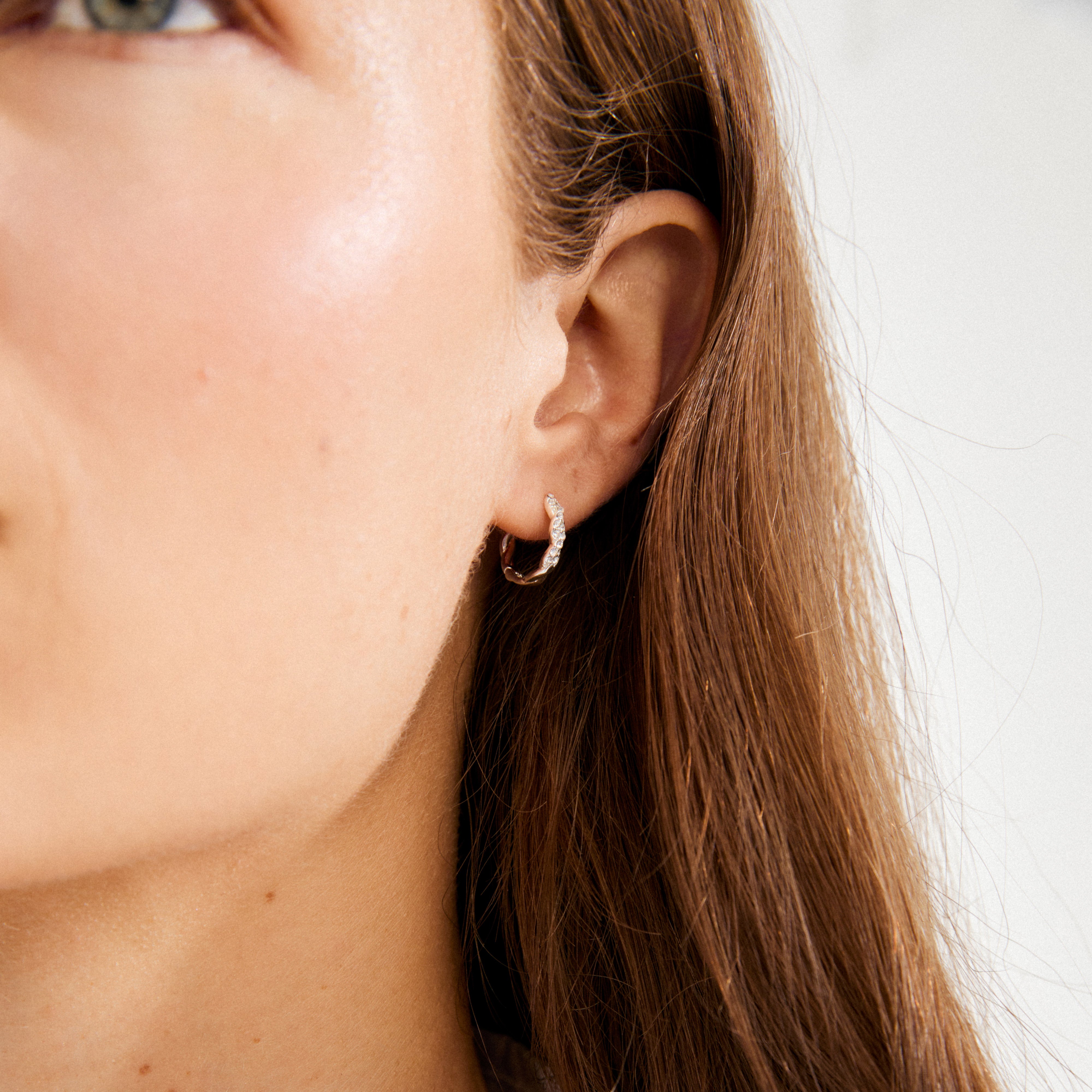 EZO twirled crystal hoops silver-plated adorn the ear, showcasing fine twisted details and shimmering Preciosa crystals against long brown hair and fair skin.