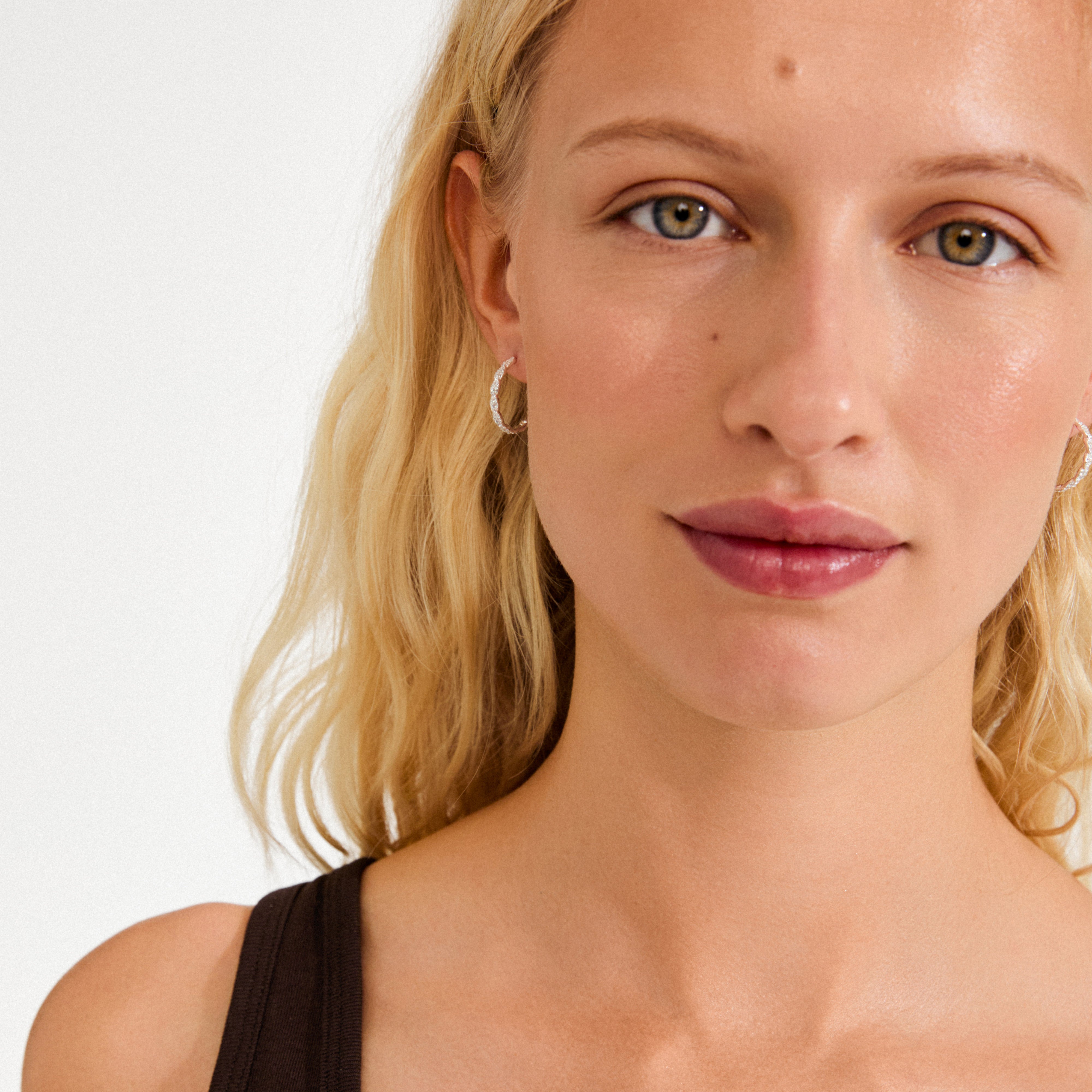 Young woman wearing EZO twirled crystal hoops, silver-plated with twisted designs and sparkling crystals, showcasing Pilgrim's blend of timeless luxury and modern style.