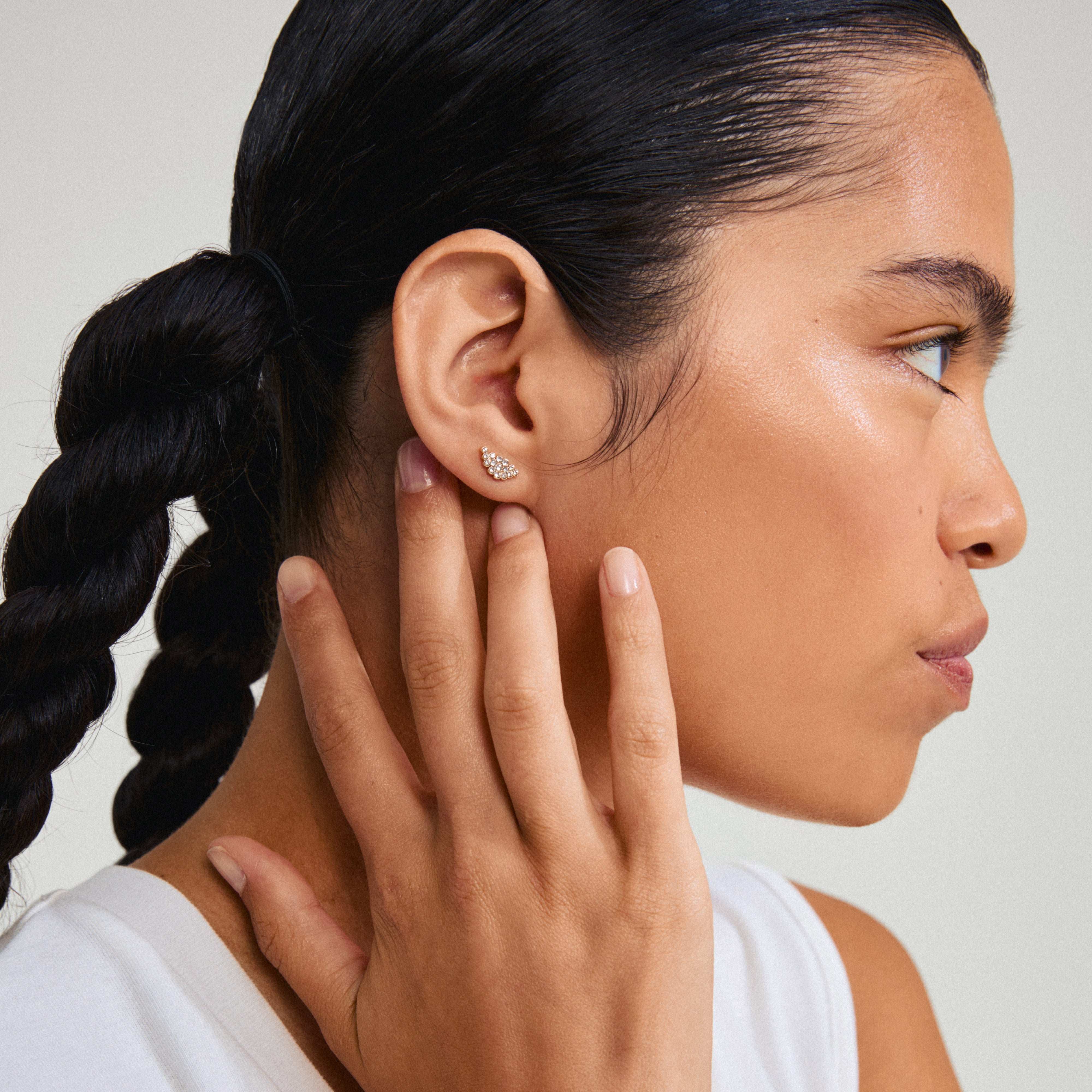 BERENIKE earrings gold-plated: A close-up of a woman's ear adorned with Pilgrim's crystal-studded gold-plated stud earrings, showcasing their elegant sparkle.