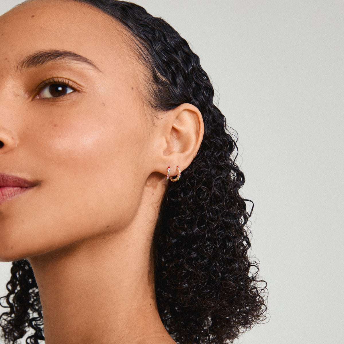 KLEOPRATRA earrings gold-plated, featuring colorful Preciosa crystals, worn by a woman with curly hair. Perfect for adding sparkle and style effortlessly.