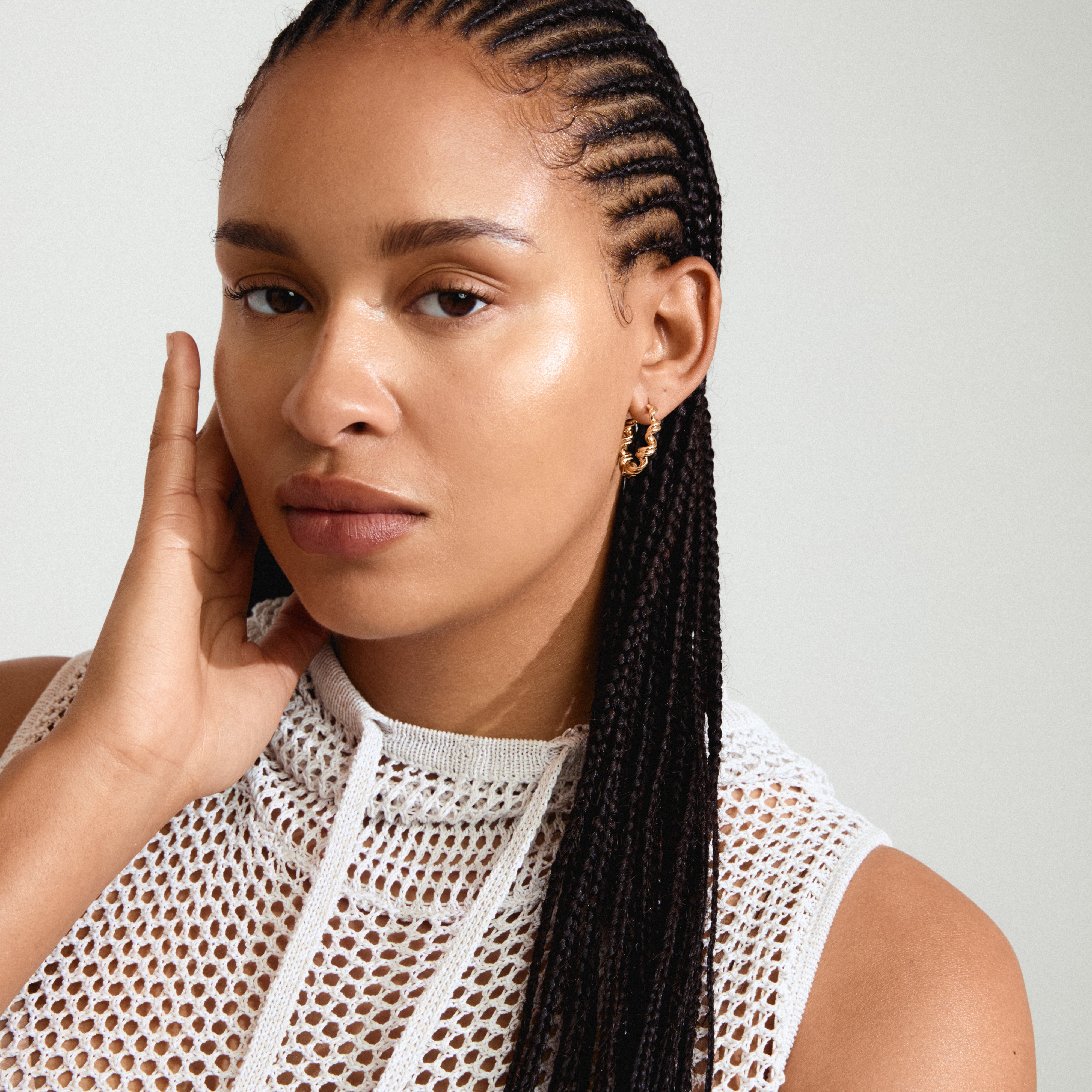 LARISA gold-plated earrings with a twisted silhouette, worn by a woman with braided hair, embodying a luxurious boho style.