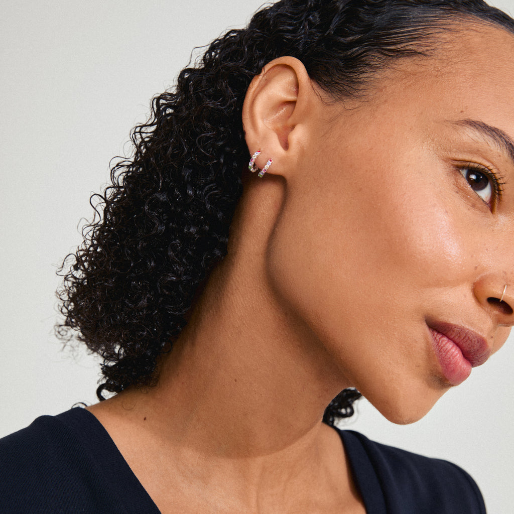 KLEOPRATRA earrings: silver-plated hoops with colorful Preciosa crystals, worn by a woman with curly hair, showcasing their sparkle and elegant design.