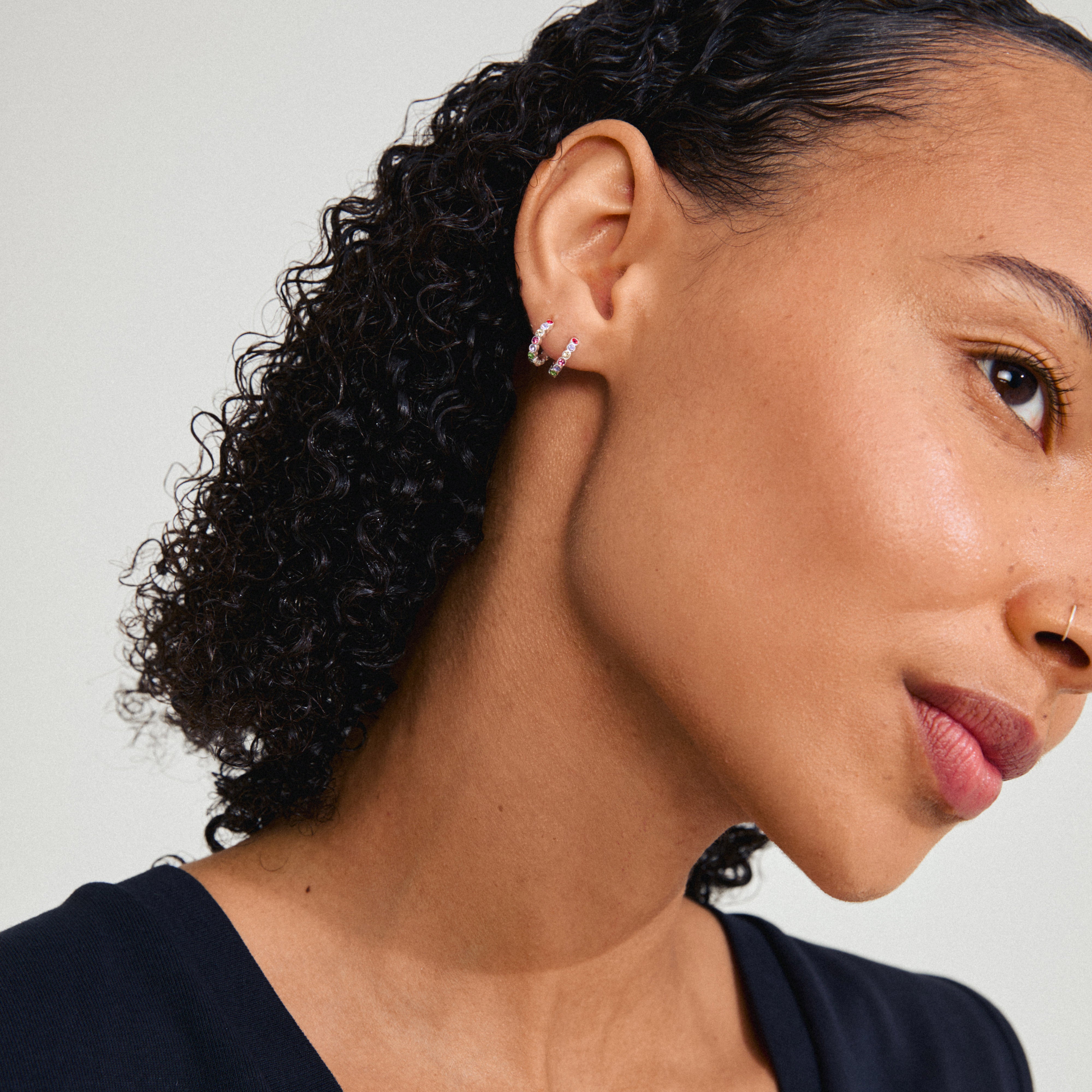 KLEOPRATRA earrings: silver-plated hoops with colorful Preciosa crystals, worn by a woman with curly hair, showcasing their sparkle and elegant design.
