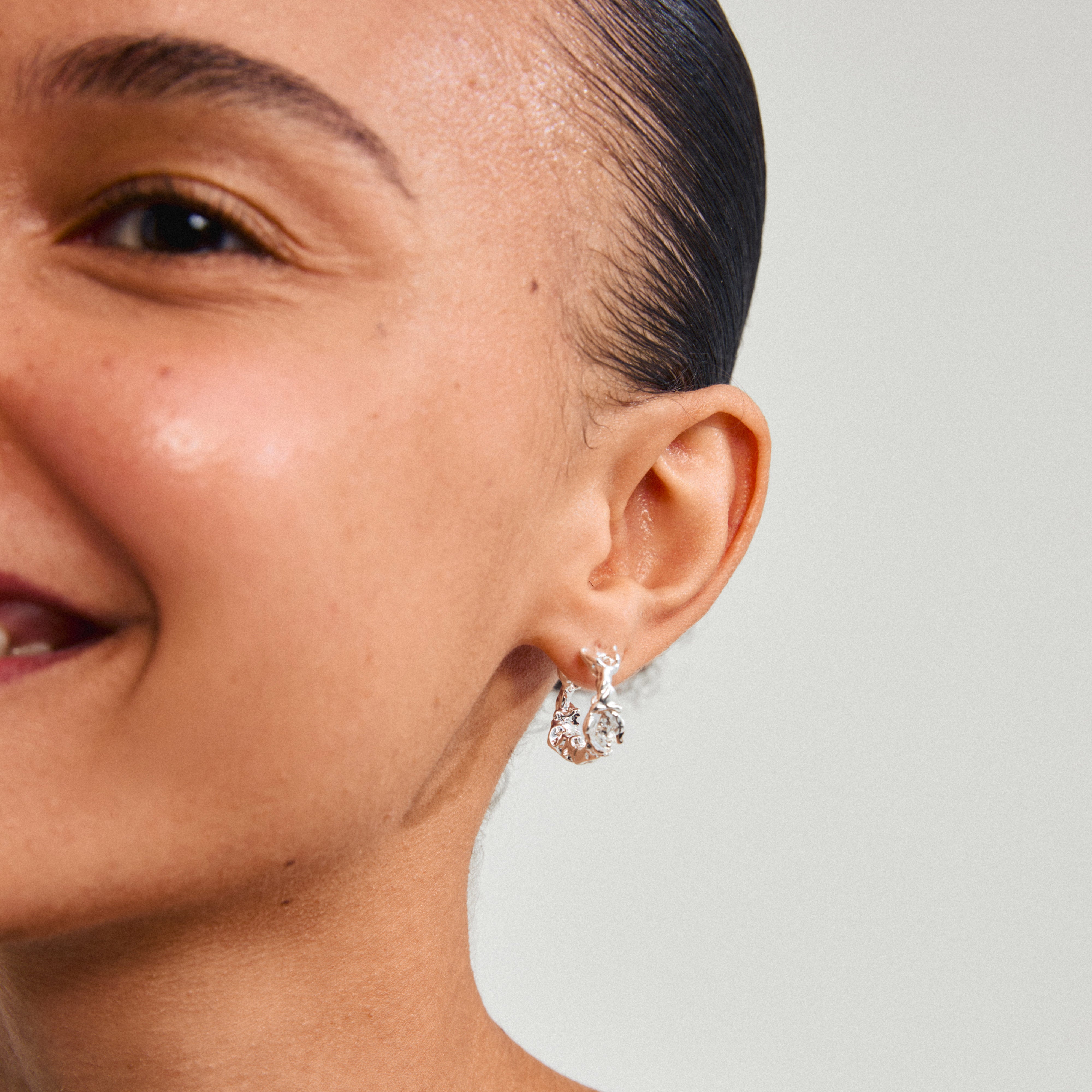 TRUST earrings silver-plated by Pilgrim, showcased as elegant silver hoops on a woman's ear, embodying timeless style and sustainability with 99% recycled materials.