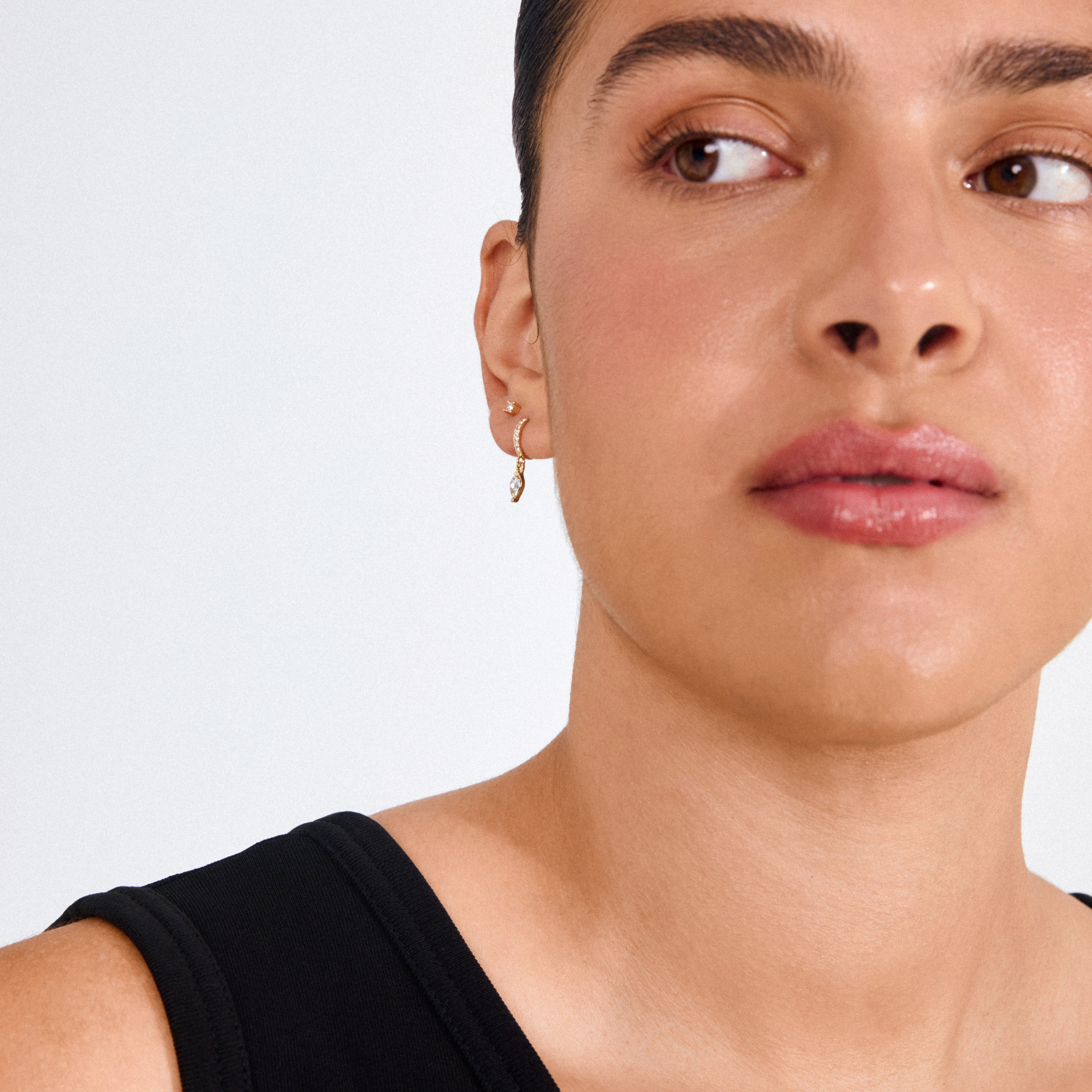 Person wearing Pilgrim's ELZA crystal earrings 2-in-1 set gold-plated, featuring a small hoop with a dangling teardrop-shaped crystal and a tiny stud above.