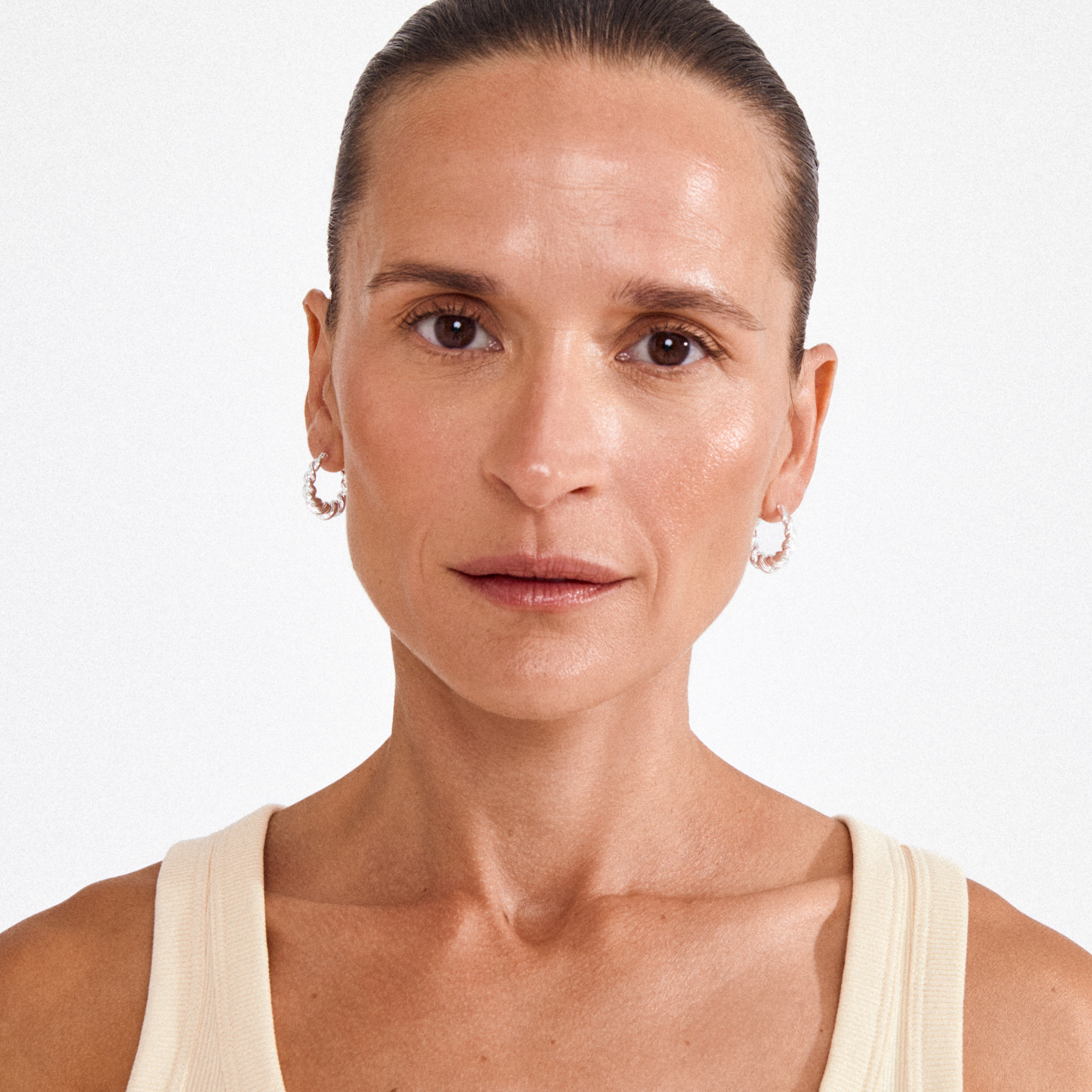 EILEEN twirl hoop earrings silver-plated adorn a woman with slicked-back hair, highlighting their twisted curves for a playful, boho-inspired style.