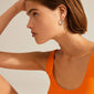 Silver-plated EILEEN huggie hoops on a woman wearing an orange tank top, showcasing elegant twisted design, inspired by waves for a boho style.