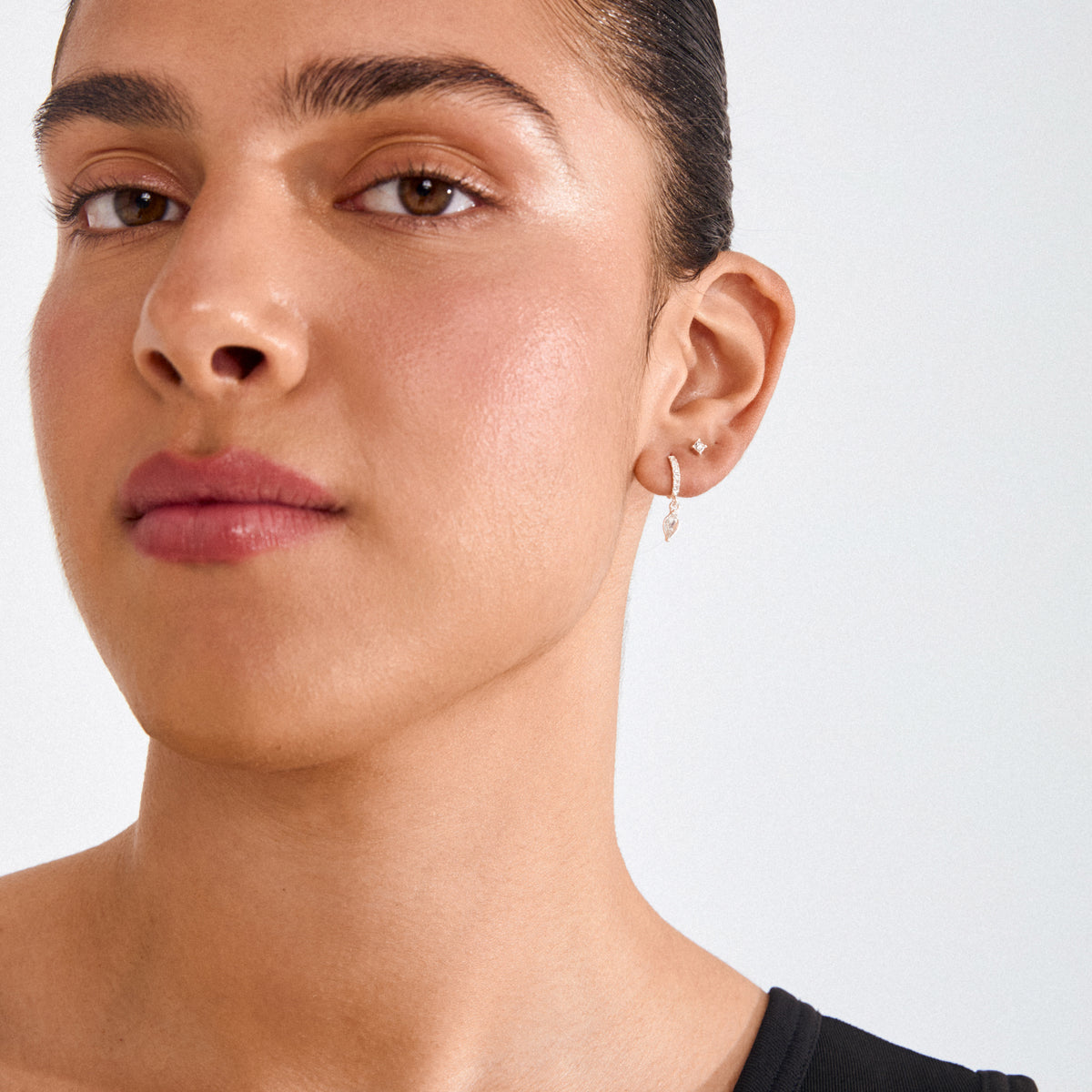 ELZA crystal earrings 2-in-1 set silver-plated, featuring a diamond-like stud and teardrop gemstone hoop, elegantly adorns a young person’s ear.
