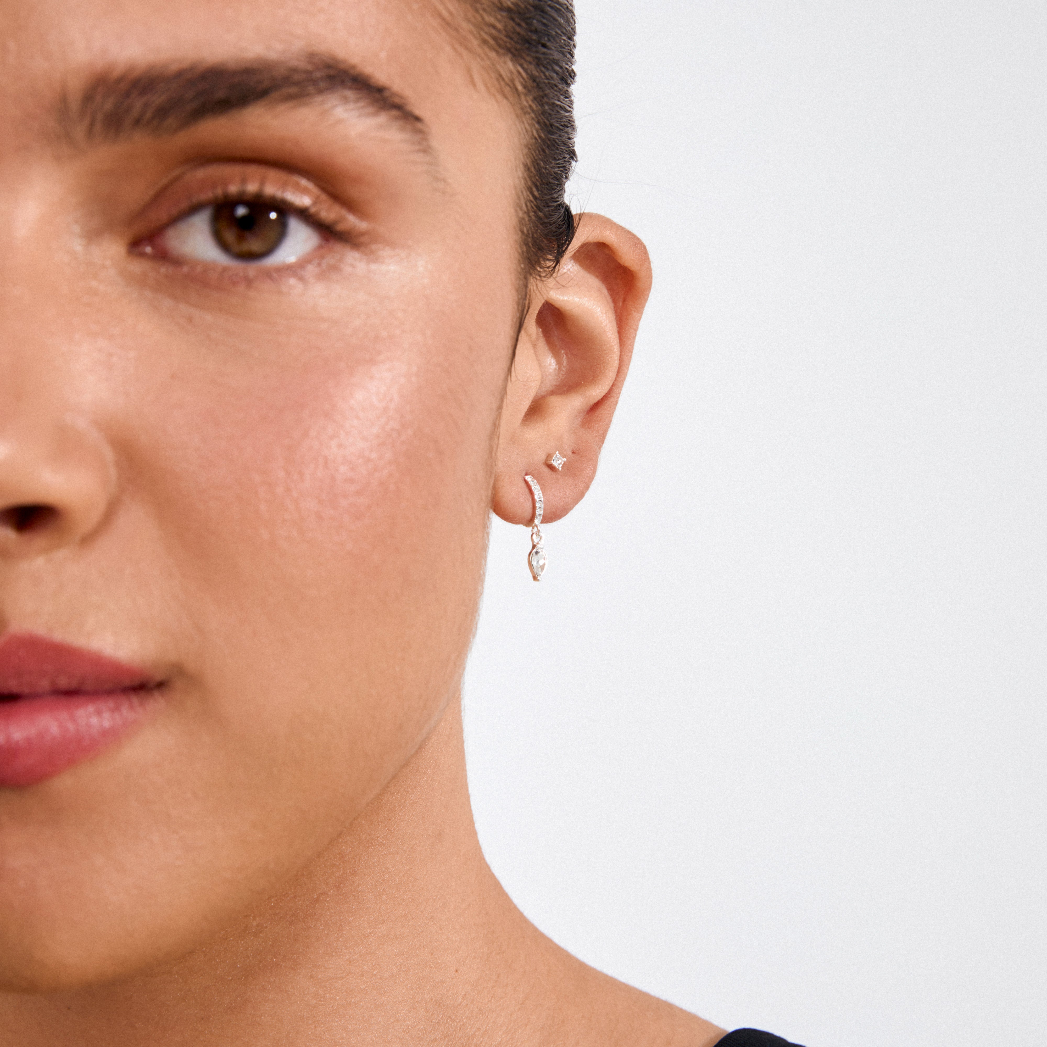 ELZA crystal earrings 2-in-1 set silver-plated, featuring a square stud and a pave-set hoop with marquise charm, elegantly adorn a woman's ear.