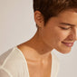 EANNA small hoops gold-plated, shown on a woman's ear, feature classic, recycled gold-plating with a simple click lock for easy stacking and personal styling.