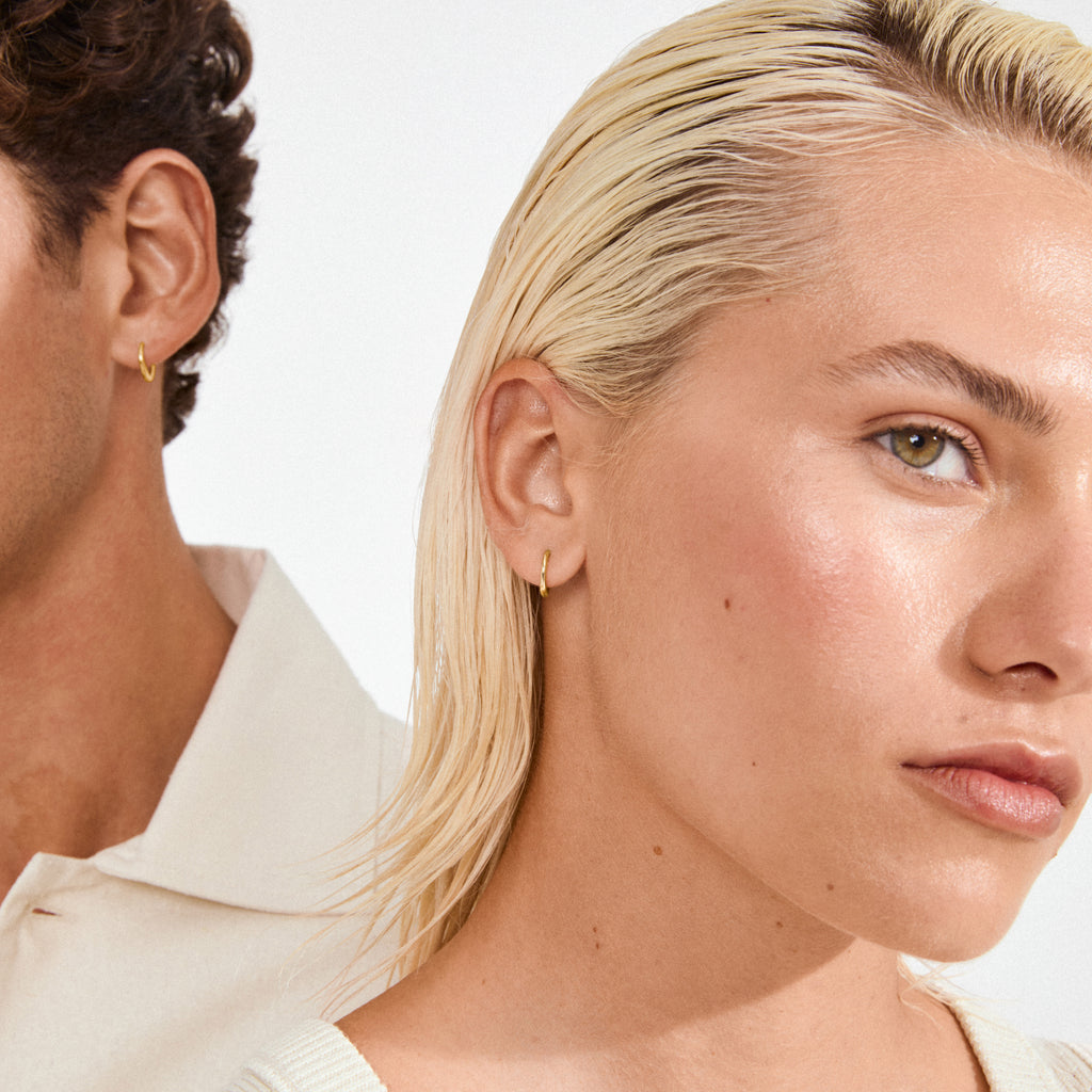Models wearing EANNA small gold-plated hoops by Pilgrim, showcasing their simplicity and elegance. Perfect for stacking, crafted from 99% recycled materials, embodying timeless style.