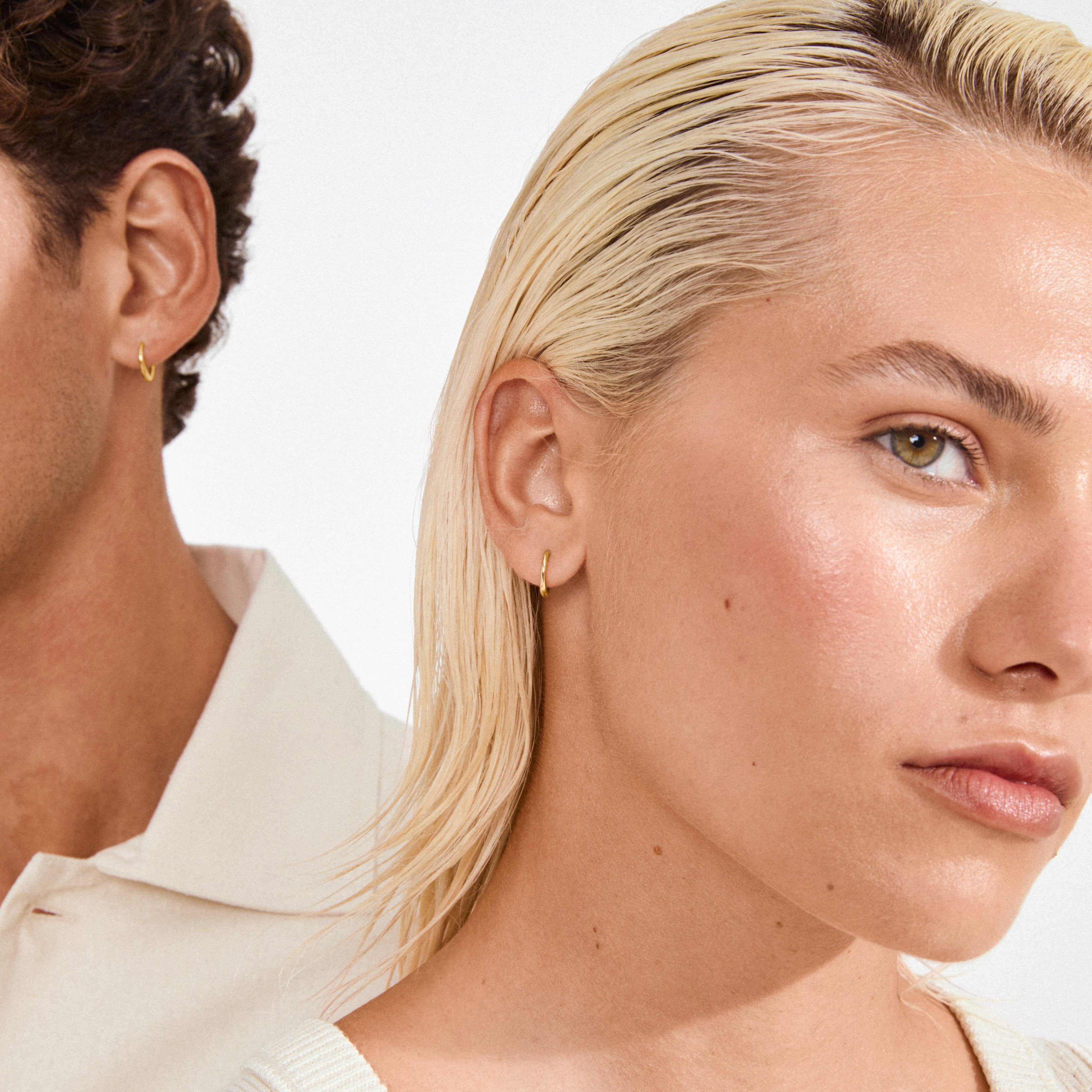 Models wearing EANNA small gold-plated hoops by Pilgrim, showcasing their simplicity and elegance. Perfect for stacking, crafted from 99% recycled materials, embodying timeless style.