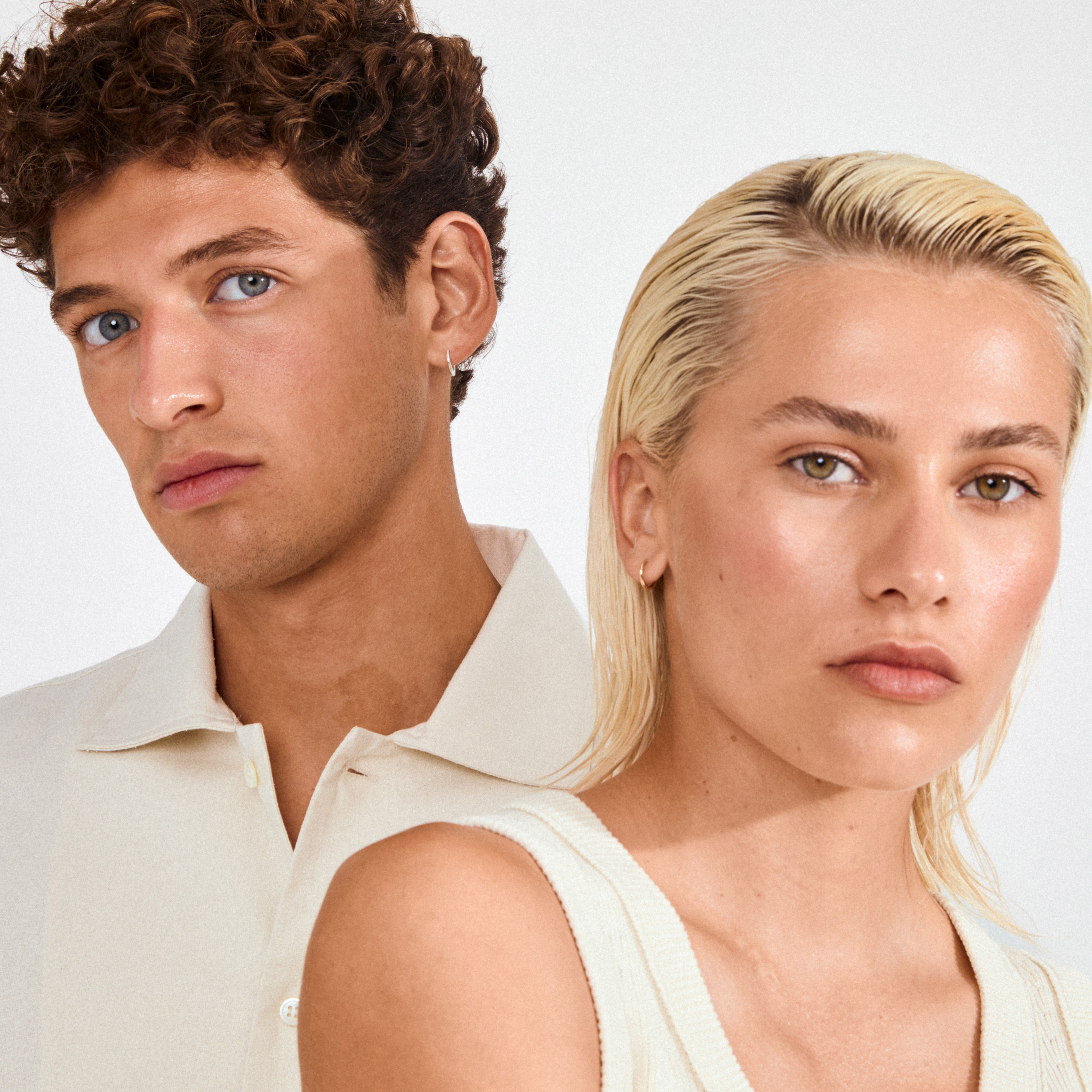 Two young adults showcase Pilgrim's EANNA small gold-plated hoops, emphasizing minimalist style and timeless elegance with their neutral expressions and natural looks.