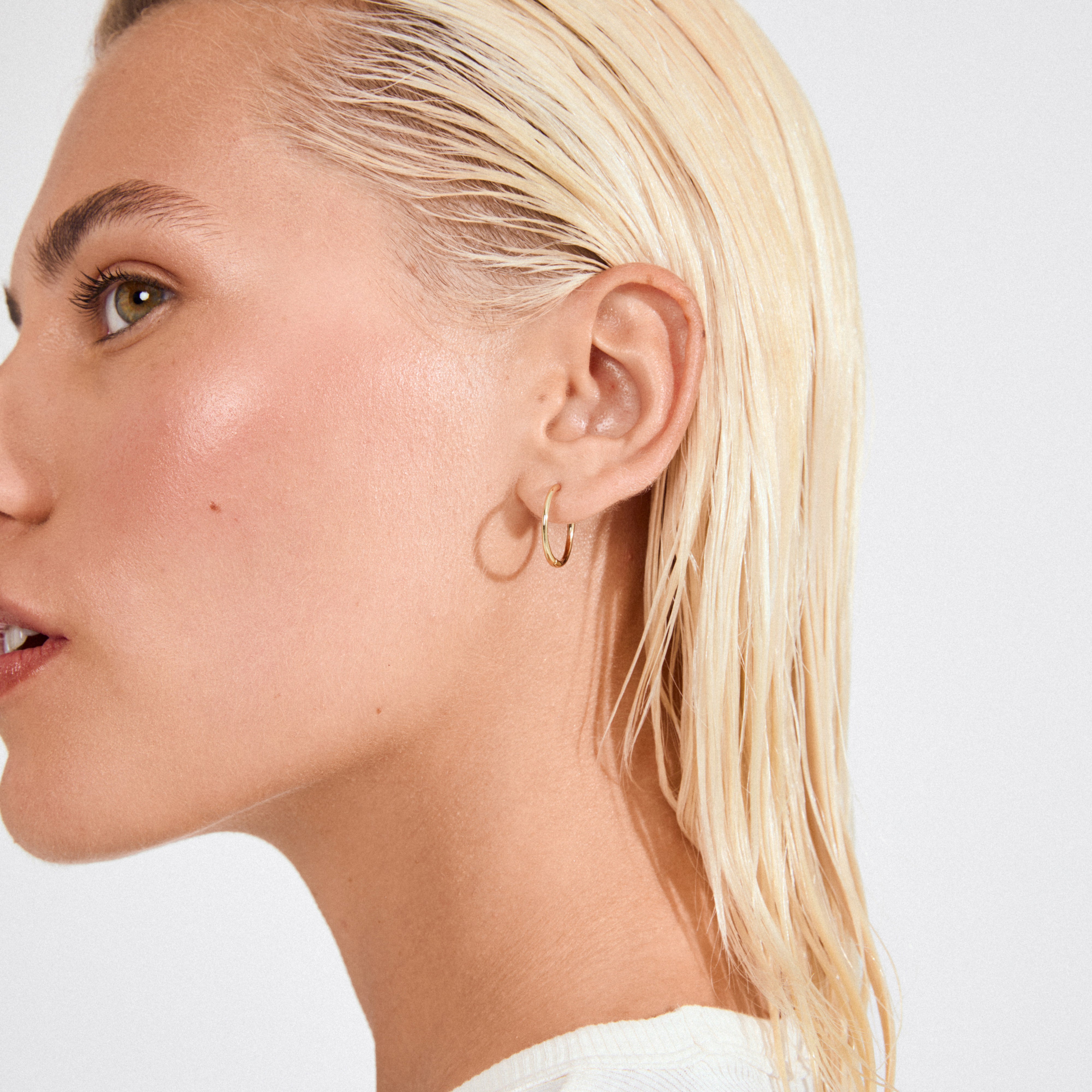 Profile view of a person wearing EANNA medium hoops gold-plated by Pilgrim, showcasing the sleek design and smooth, dewy skin.