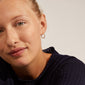 Woman smiling wearing EANNA medium gold-plated hoop earrings from Pilgrim, showcasing their elegant design with a smart click lock for easy wear.