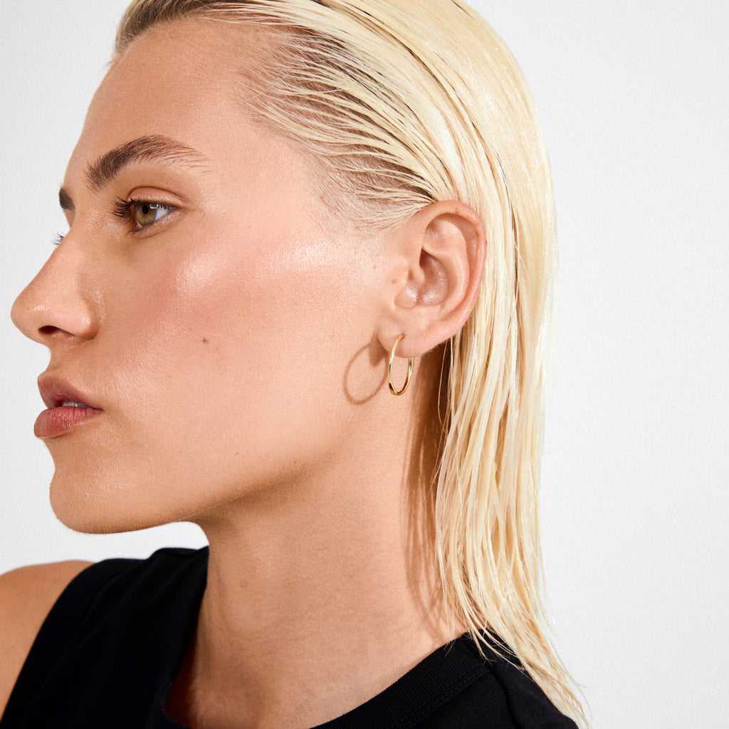 Close-up of person wearing EANNA large gold-plated hoops, showcasing their sleek, elegant design, perfect for versatile styling and crafted from 99% recycled materials.