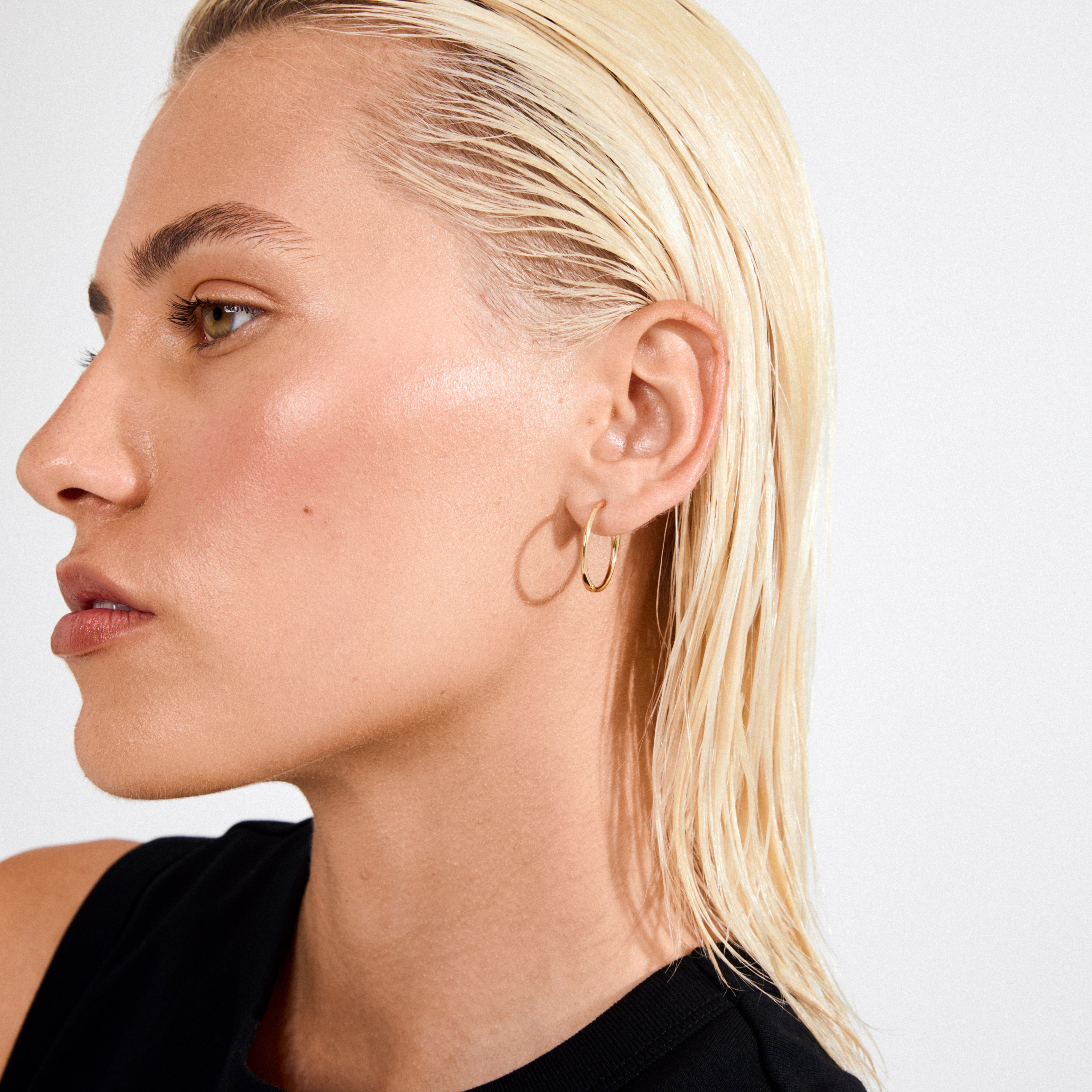 Close-up of person wearing EANNA large gold-plated hoops, showcasing their sleek, elegant design, perfect for versatile styling and crafted from 99% recycled materials.