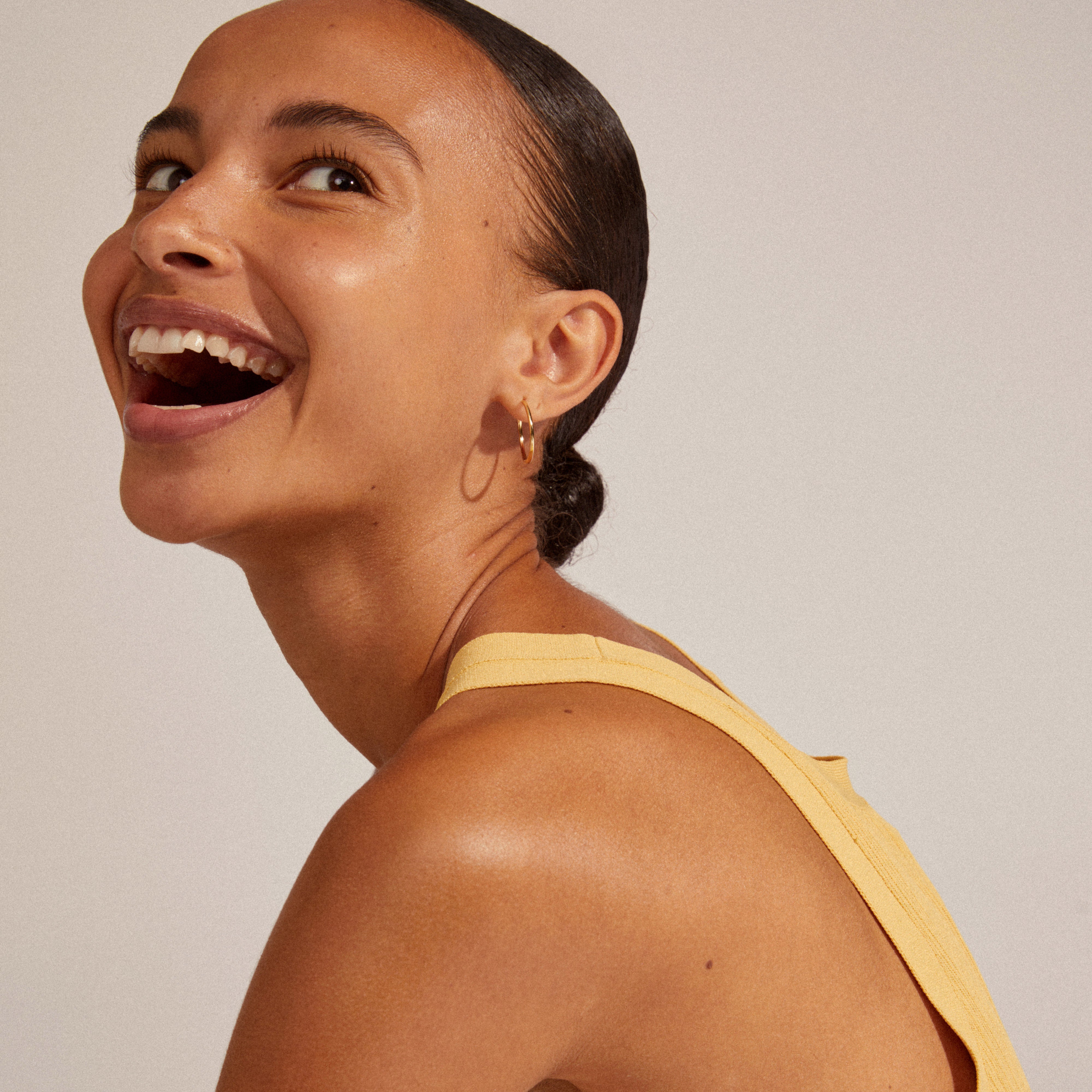A woman joyfully wearing EANNA large gold-plated hoops, showcasing their elegant design and simplicity, perfect for personal styling and versatile jewelry collections.