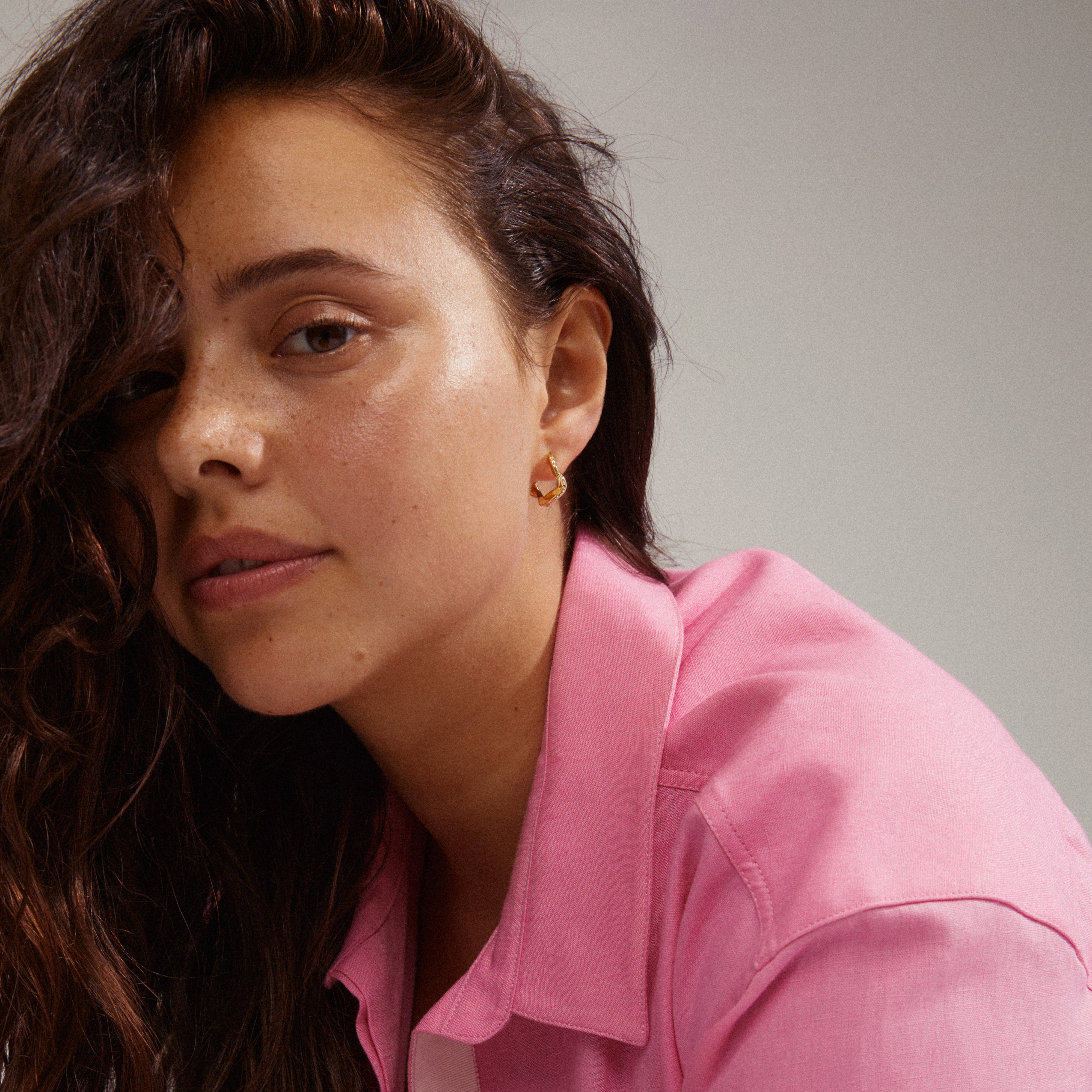 Evra gold-plated hoops with organic curves and Preciosa crystals, designed for a stylish, modern look, worn by a woman with long brown hair.