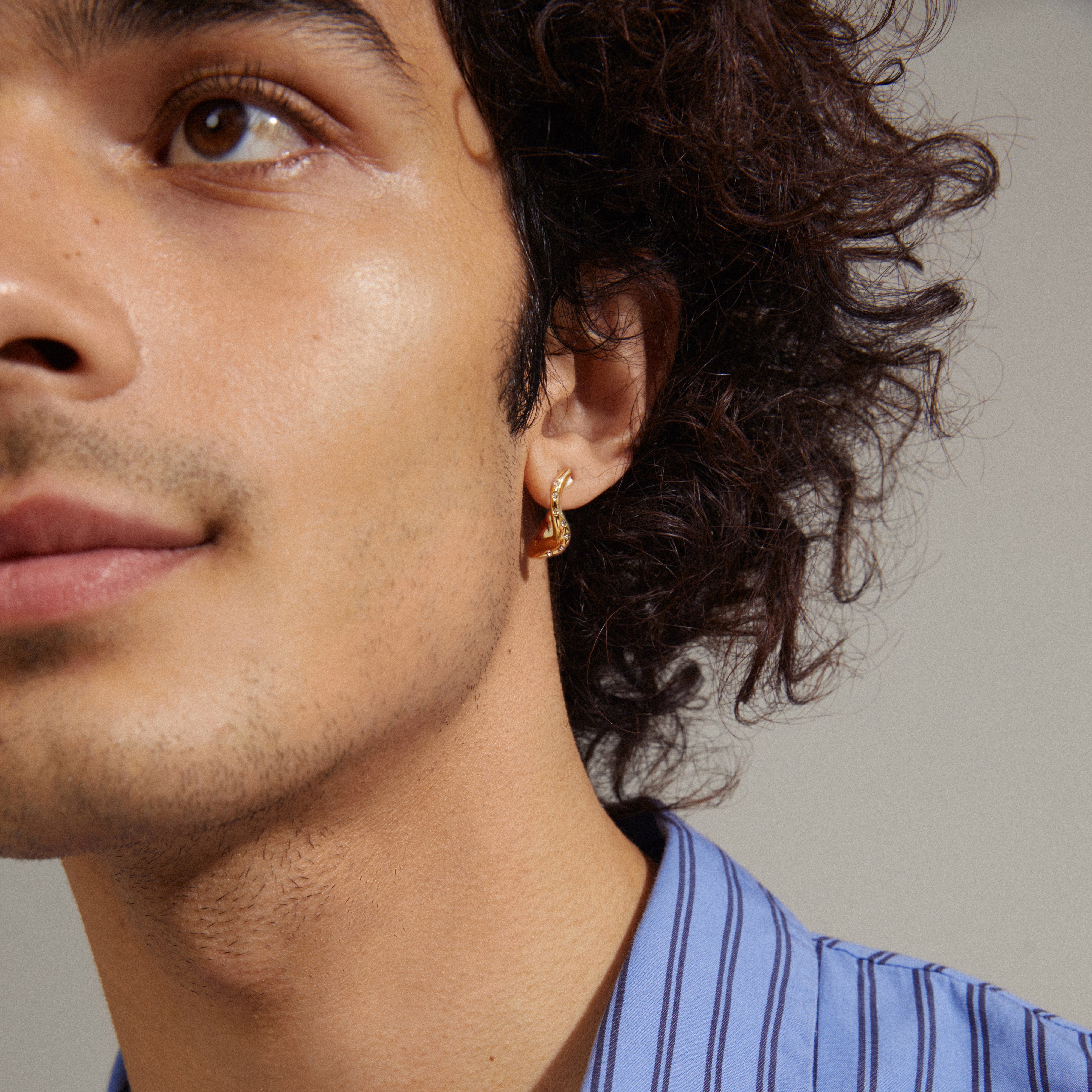 Close-up of a man's ear wearing Evra organic-shaped crystal hoops, gold-plated, showcasing their wavy design and discreet shine with Preciosa crystals.