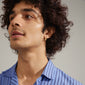 Man wearing blue striped shirt showcasing Evra organic shaped gold-plated crystal hoops. The earrings feature a wavy design and discreet shine, highlighting their elegant craftsmanship.
