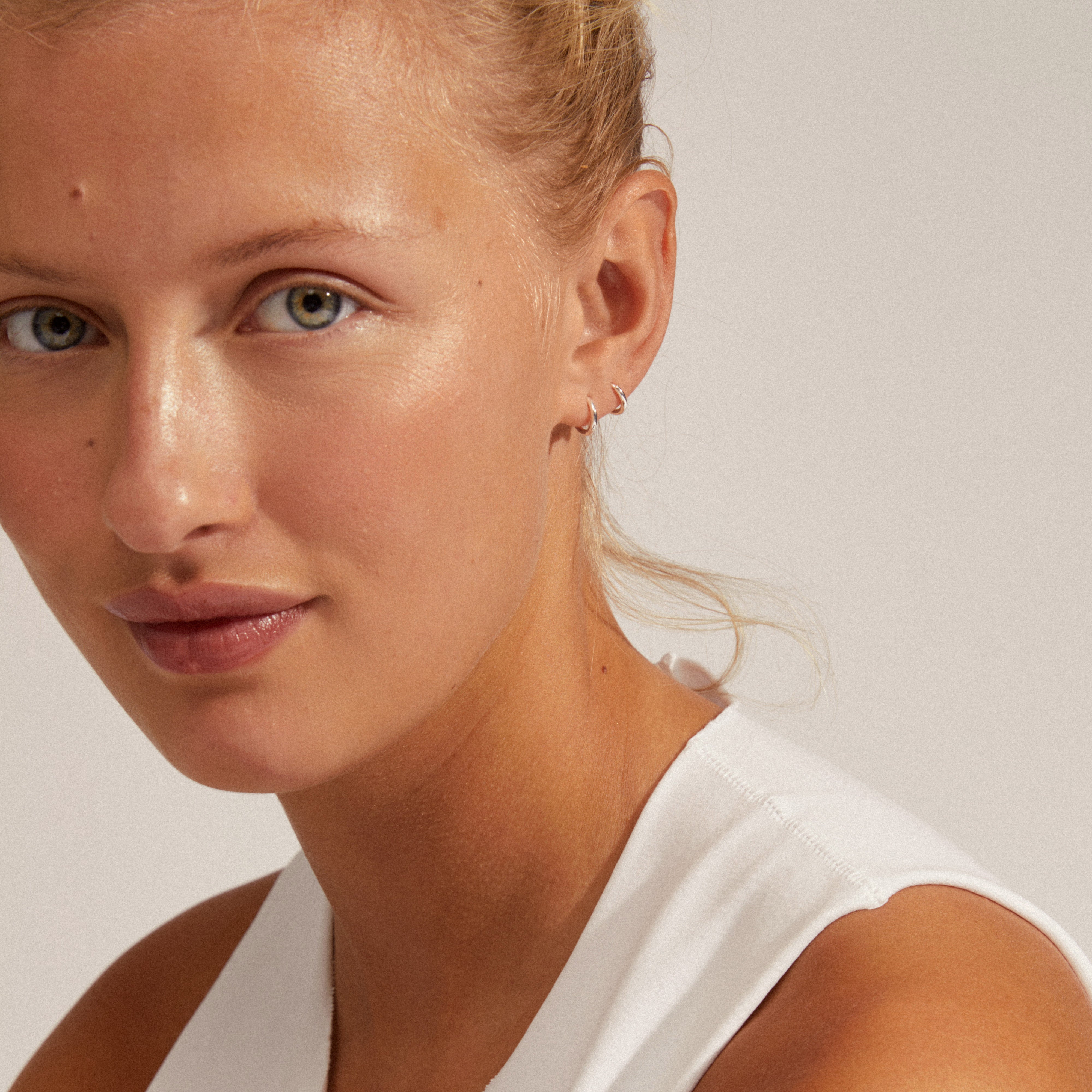 Woman wearing EANNA huggie hoops silver-plated, showcasing their wider silhouette and classic design. Perfect for pairing with other jewelry pieces.