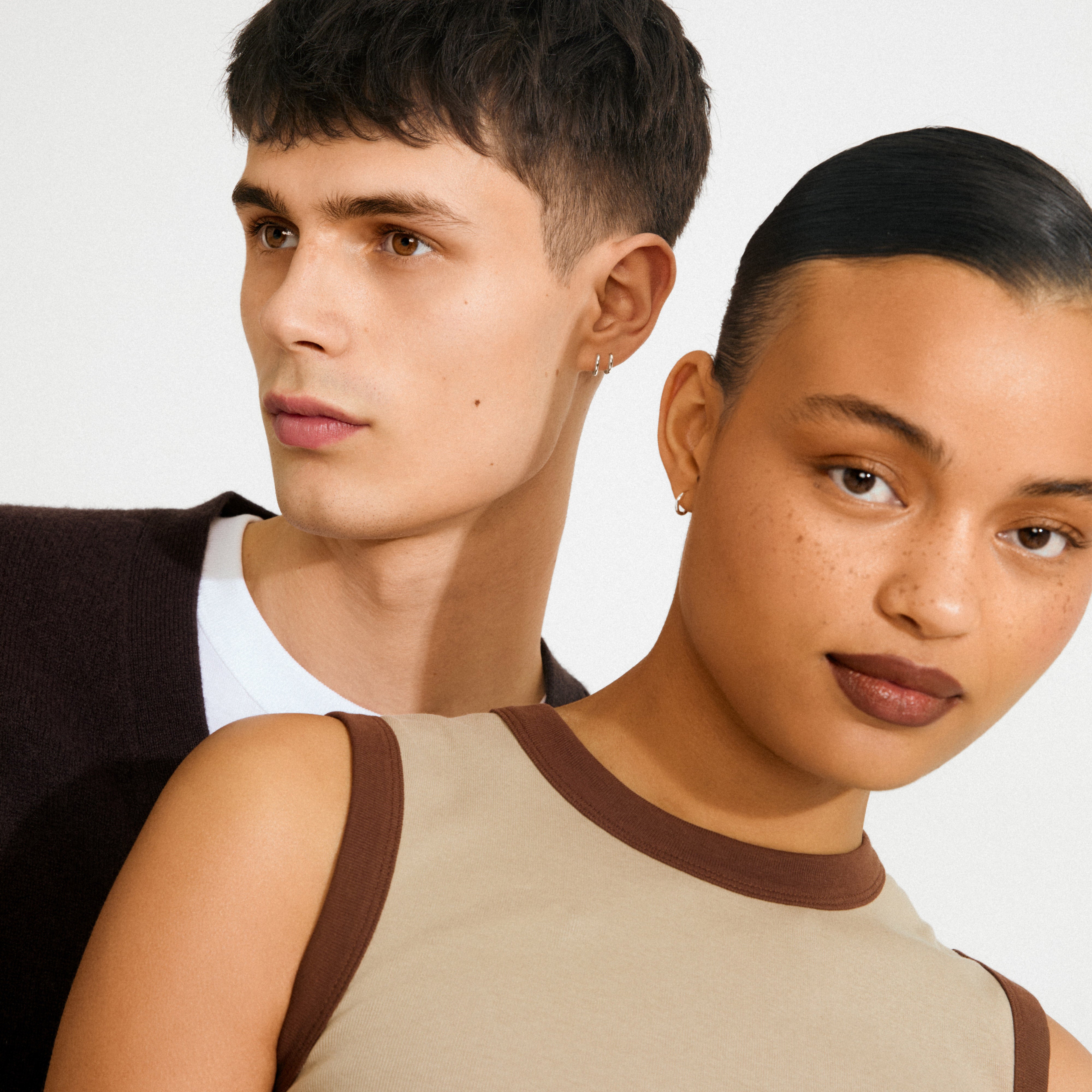 Two young adults model EANNA huggie hoops silver-plated earrings, showcasing their timeless yet trendy design with small hoop silhouettes and easy click locks.