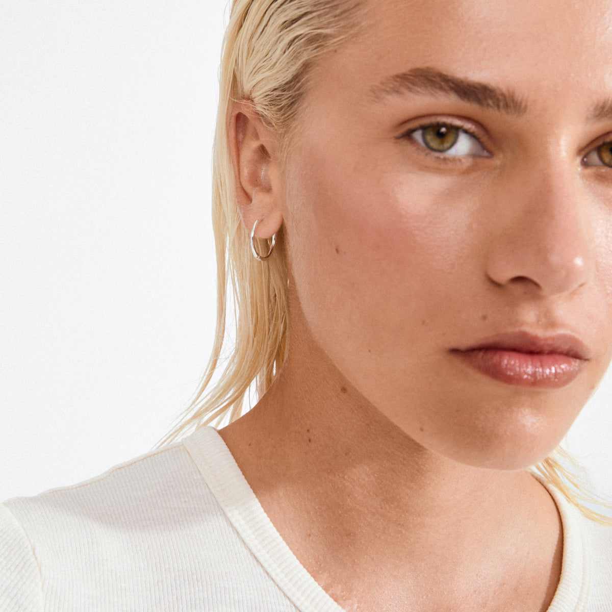 Close-up of a young person wearing EANNA medium hoops silver-plated, showcasing the elegant, recycled silver hoop earring against a sleek, minimalist backdrop.