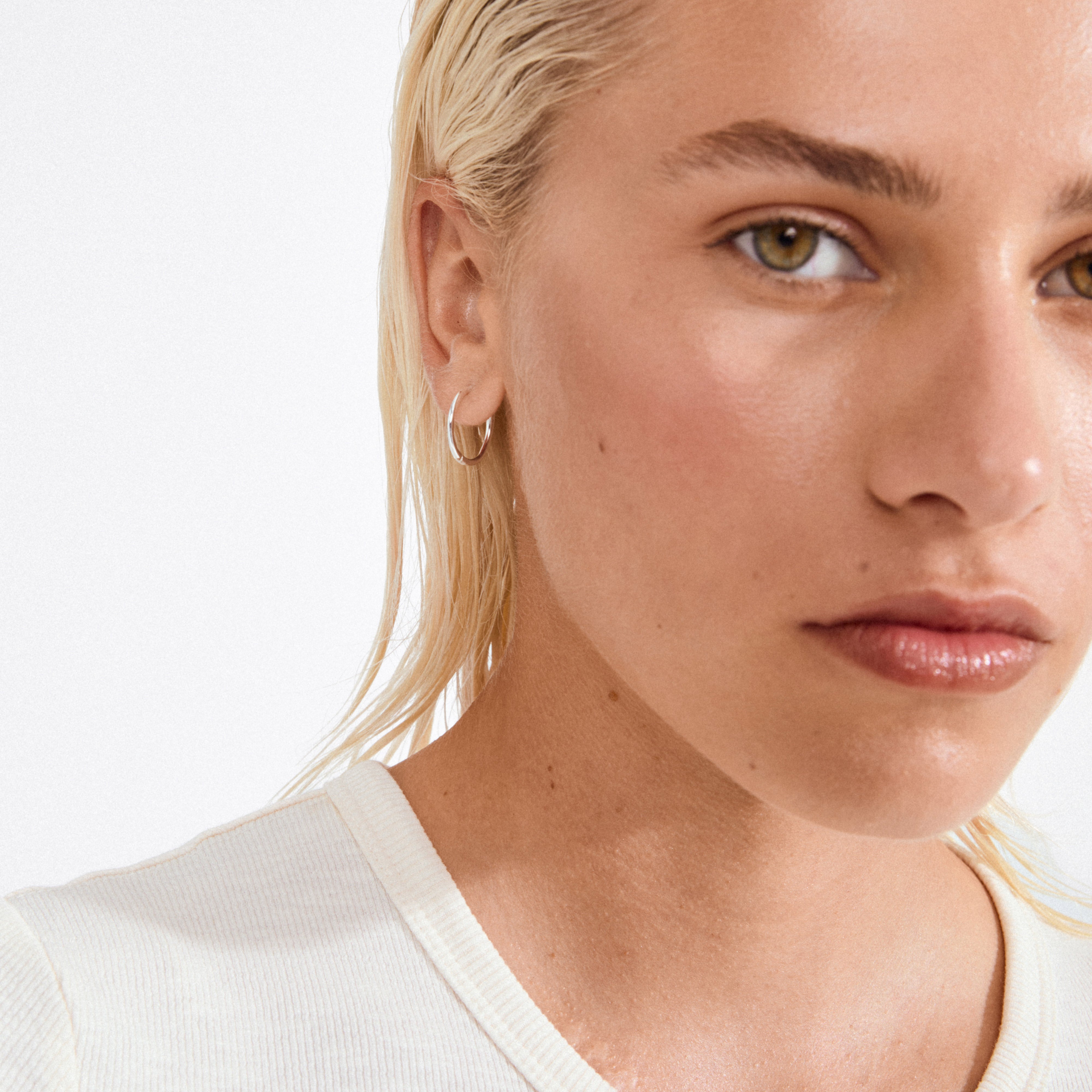 Close-up of a young person wearing EANNA medium hoops silver-plated, showcasing the elegant, recycled silver hoop earring against a sleek, minimalist backdrop.