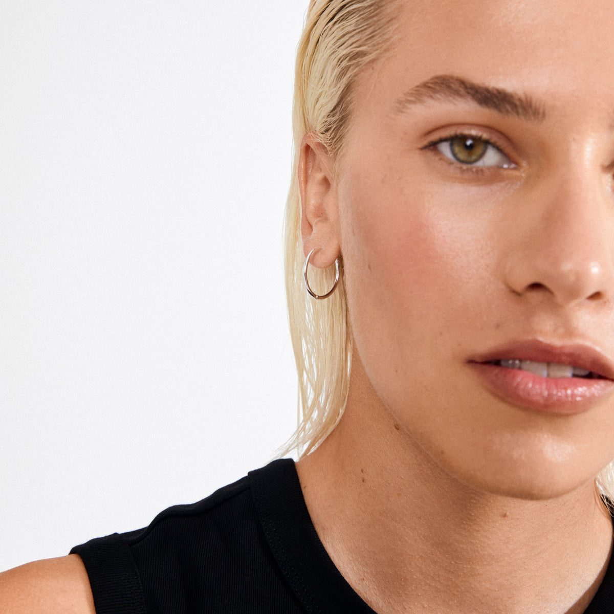 Person wearing EANNA large hoops silver-plated earrings, showcasing their wide silhouette and timeless style, paired with a black sleeveless top.