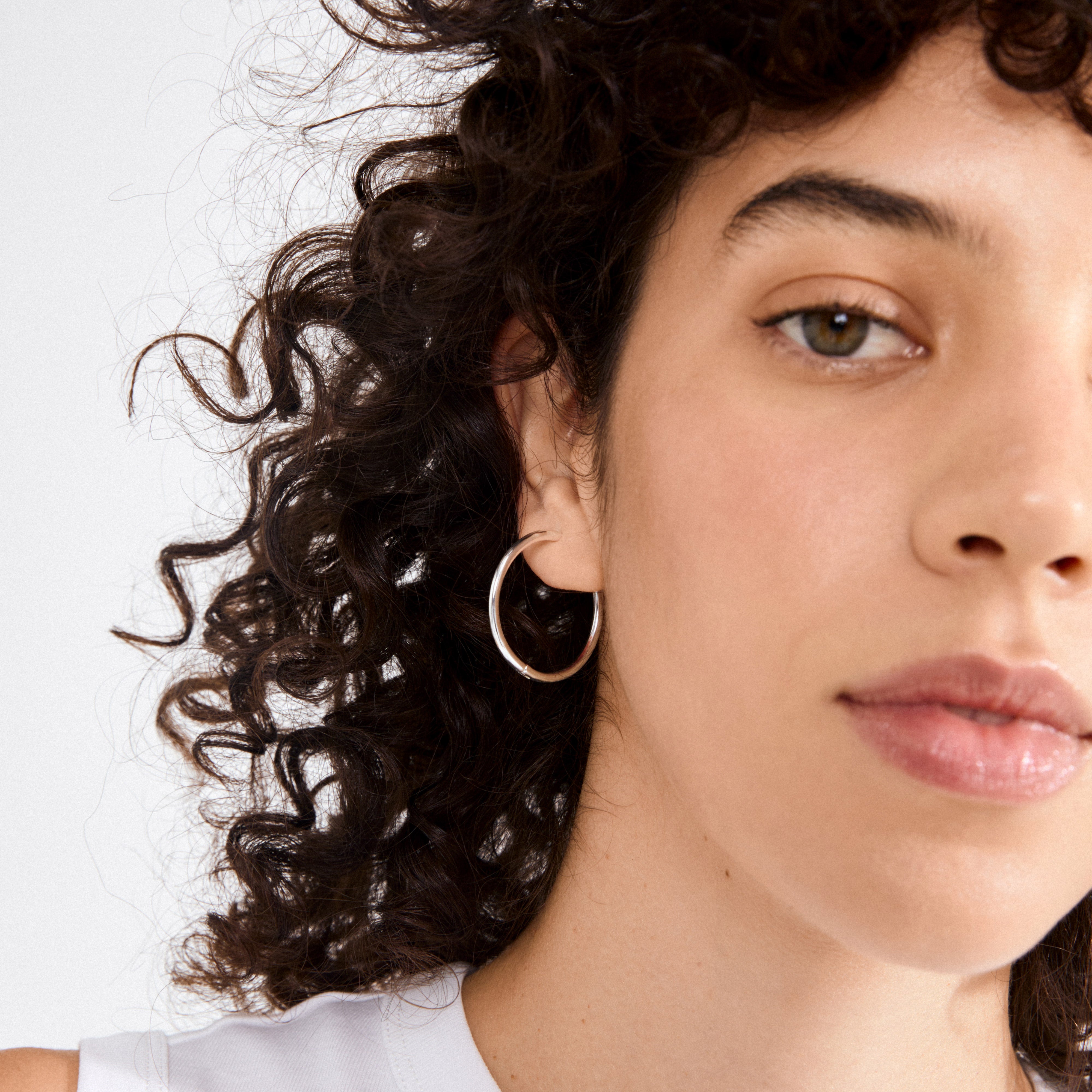 Close-up of a young person wearing EANNA maxi hoops silver-plated, showcasing the hoop's elegant design against their smooth skin and simple makeup.
