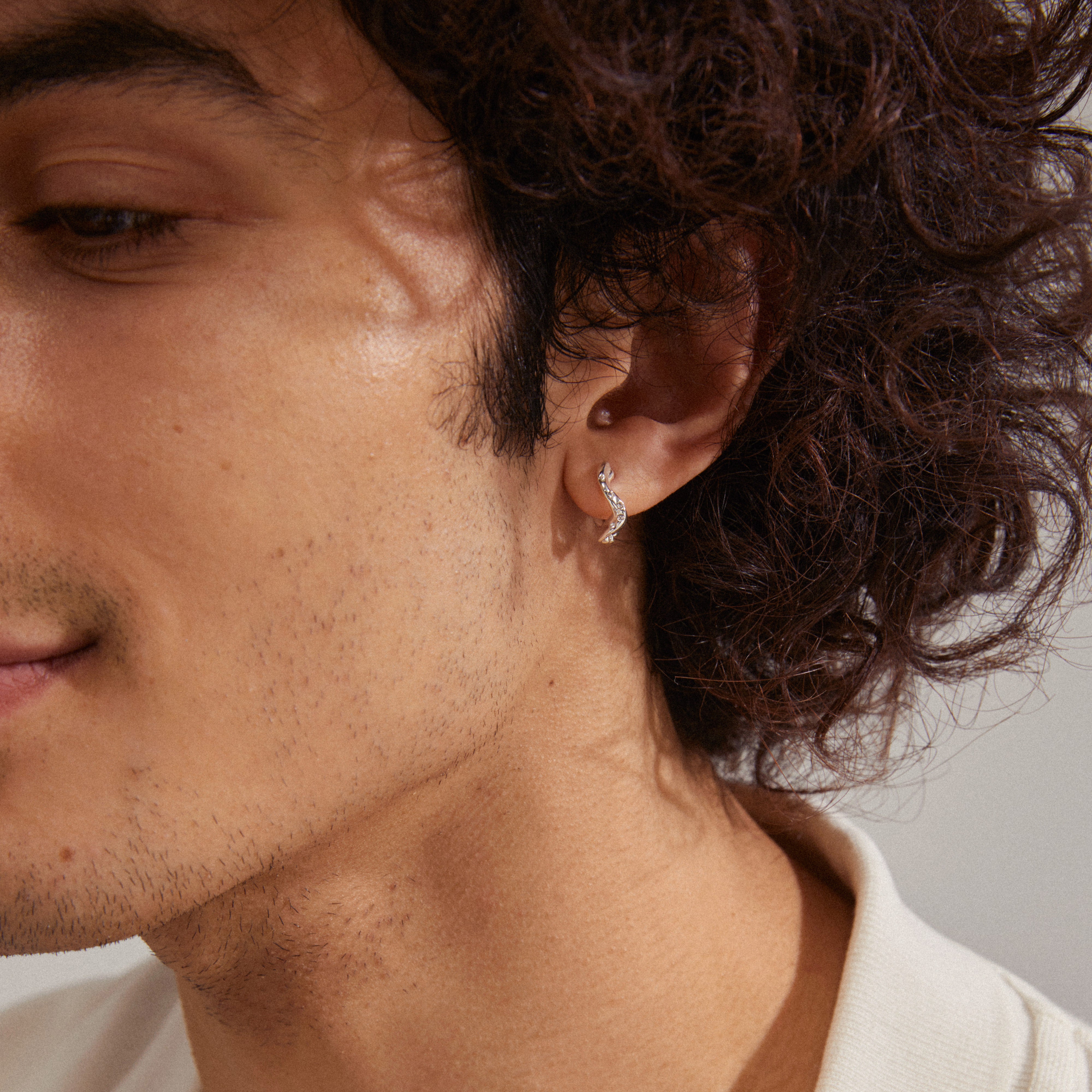 Close-up of a man's ear showcasing EVRA organic shaped crystal hoops, silver-plated, with handcrafted design and sparkling Preciosa crystals.
