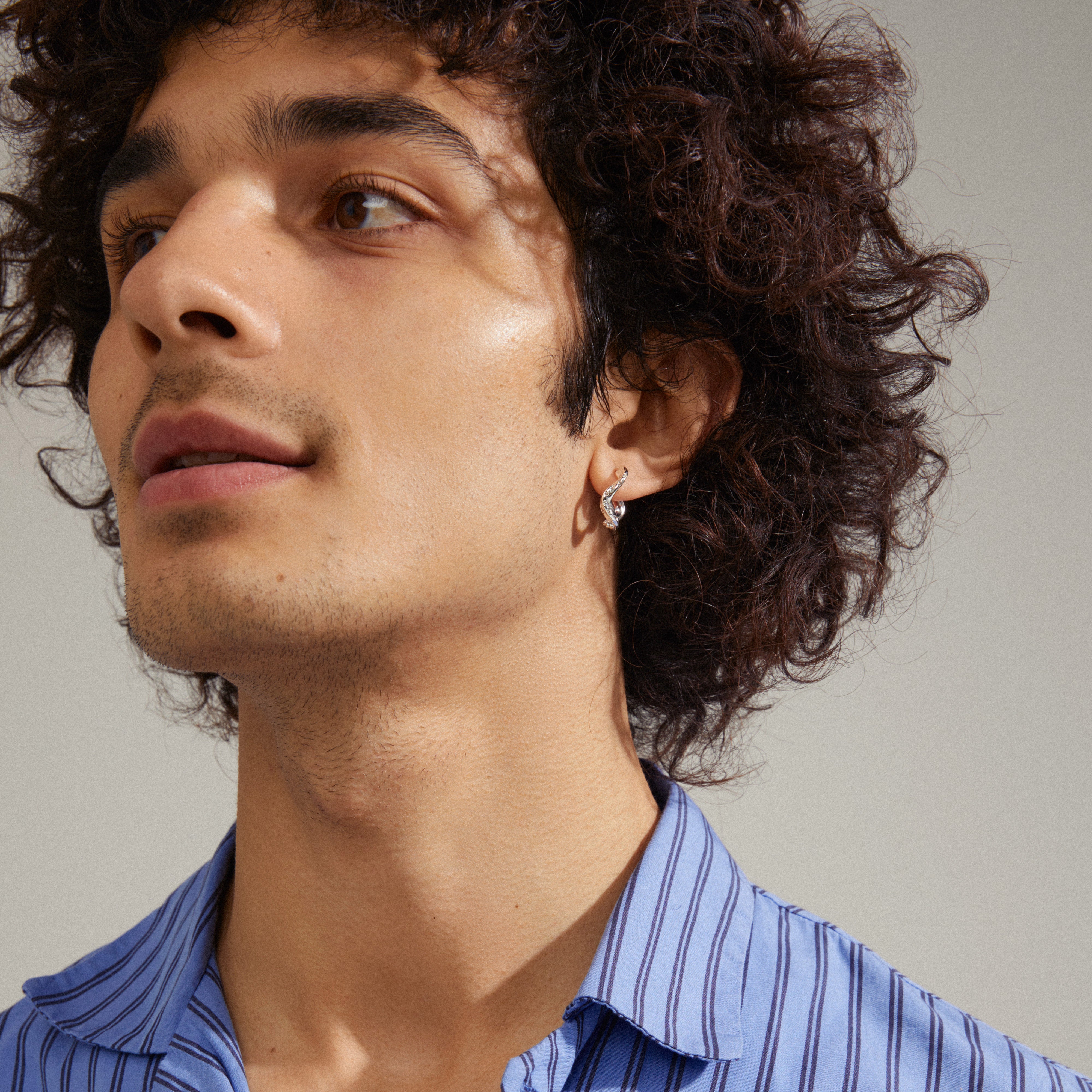 Man wearing blue striped shirt showcasing the EVRA organic shaped crystal hoops, silver-plated, with a handcrafted look and sparkling Preciosa crystals.