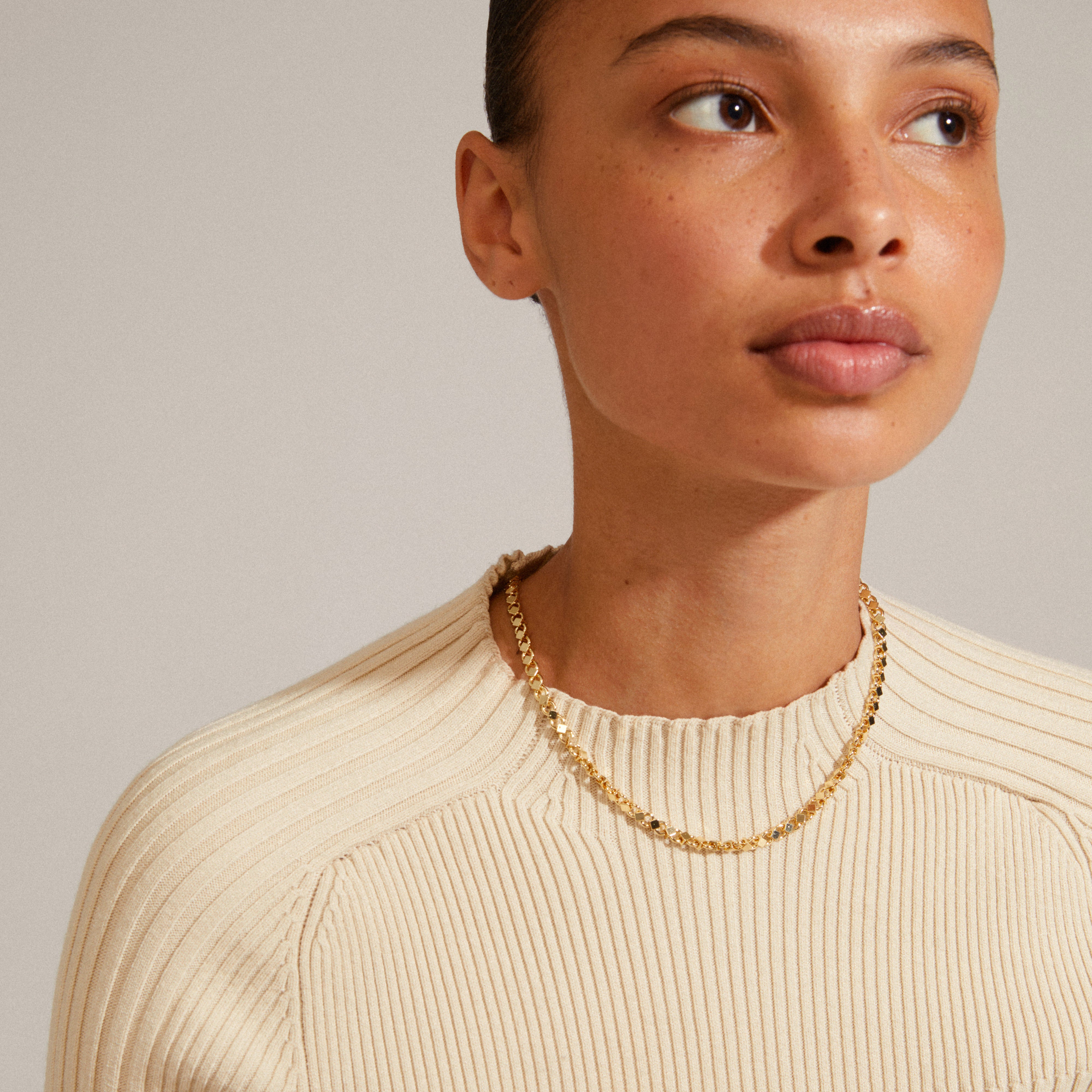 Close-up of a woman wearing the gold-plated DESIREE necklace, showcasing its unique cube and round link design.