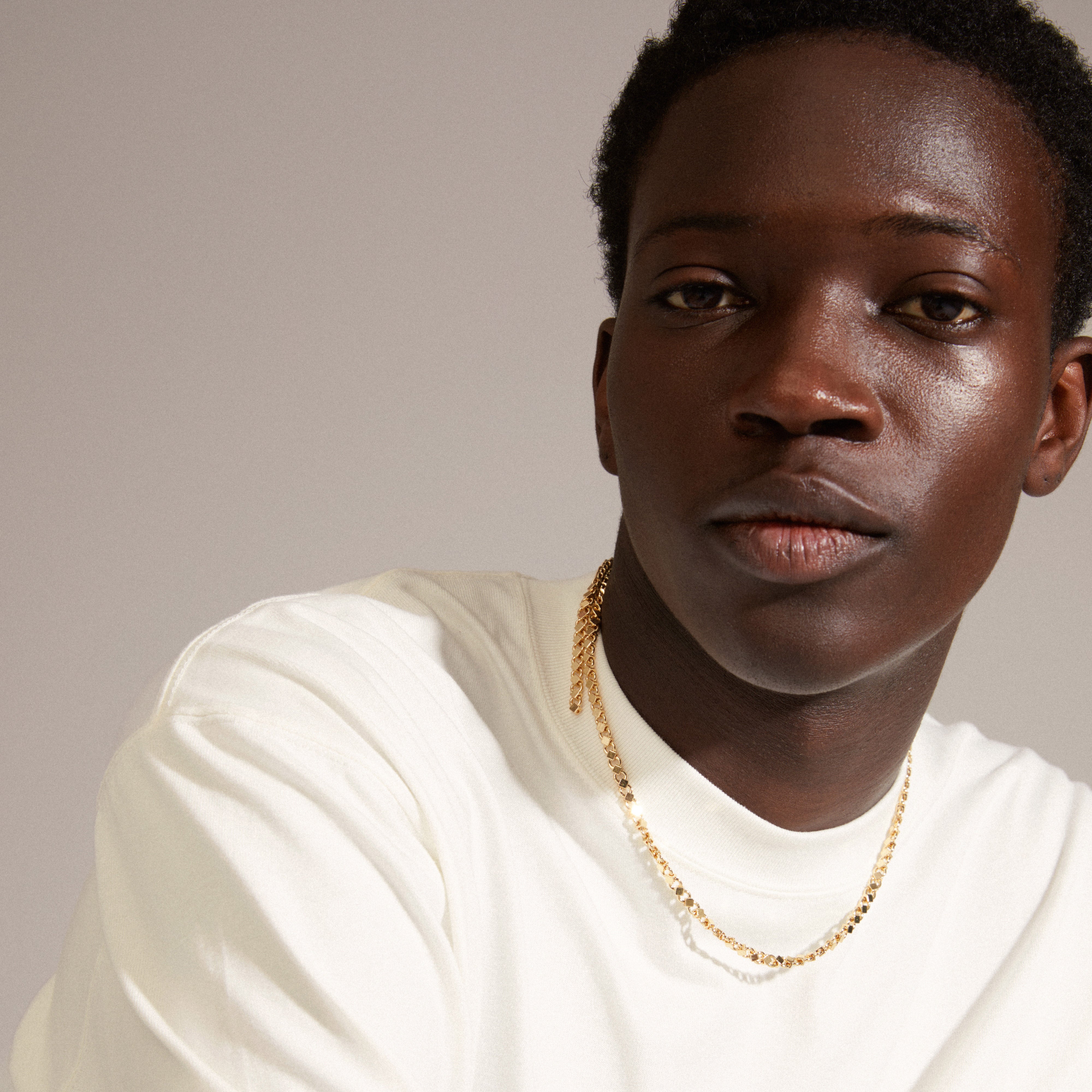 Man wearing a white shirt showcasing the gold-plated DESIREE necklace from Pilgrim, featuring a unique chain design with cubes and round links.