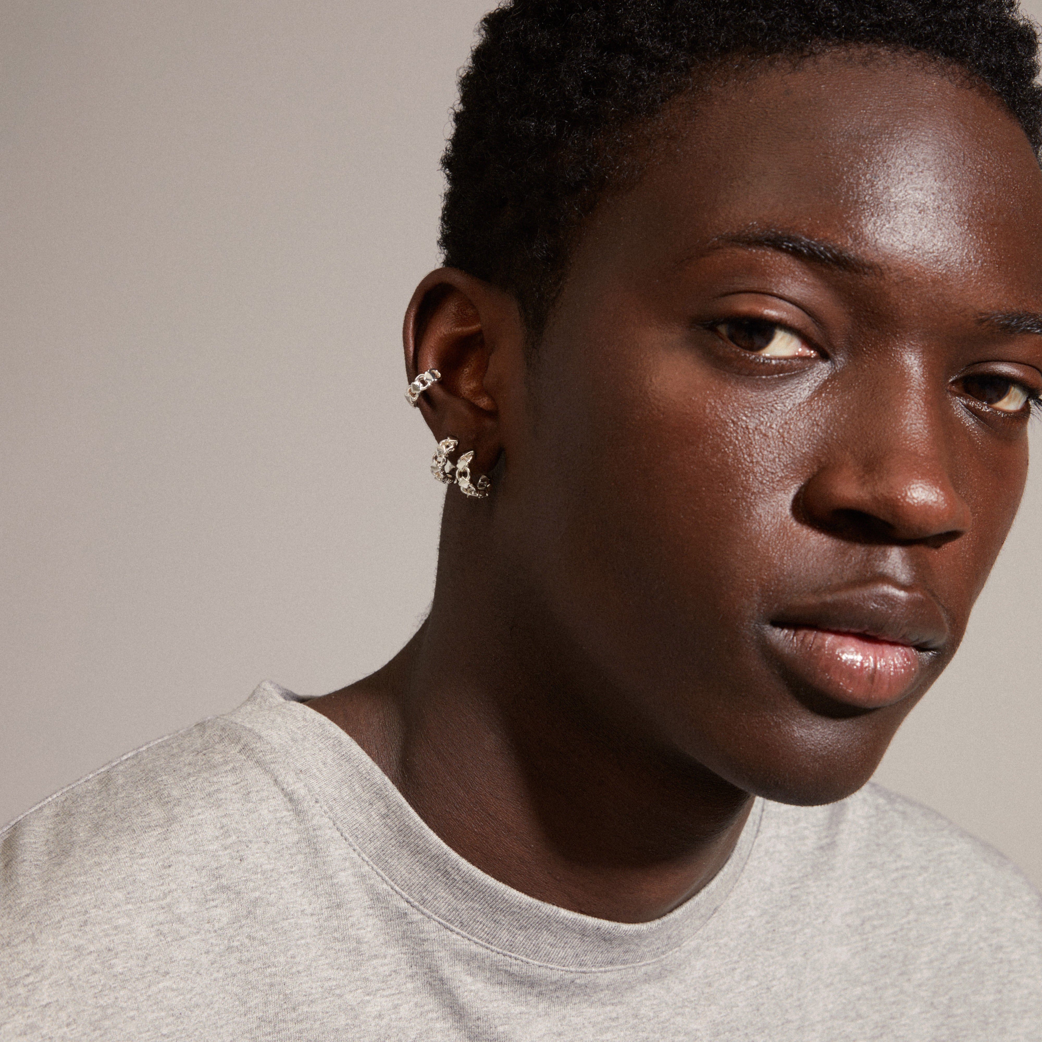 DESIREE silver-plated huggie hoops and ear cuffs with unique chain design, featuring cubes and round links. Modeled by a man, showcasing trendy style.