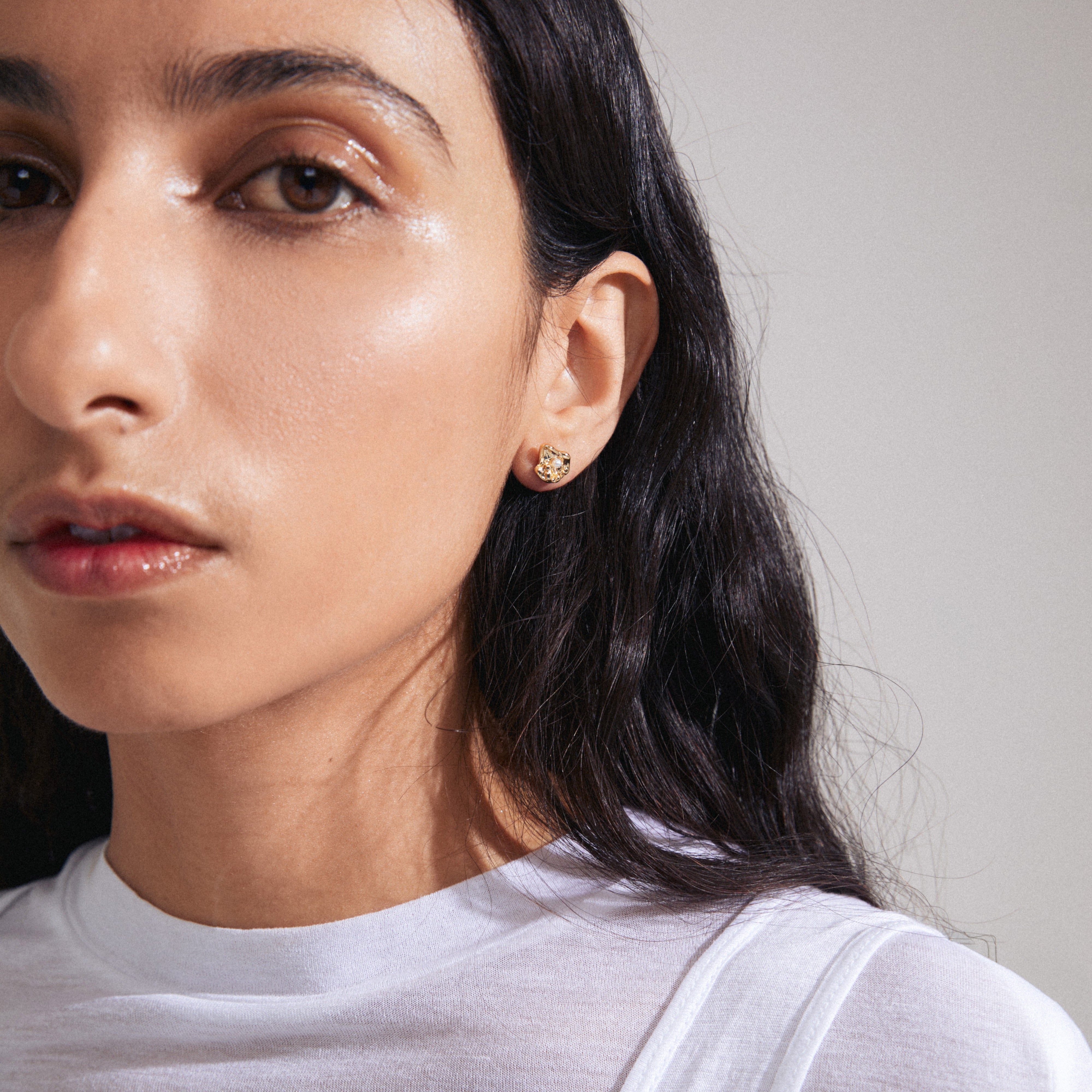 INAYA earrings gold-plated by Pilgrim, featuring abstract seashell-shaped studs with a central white glass bead, crafted from 96% recycled materials.