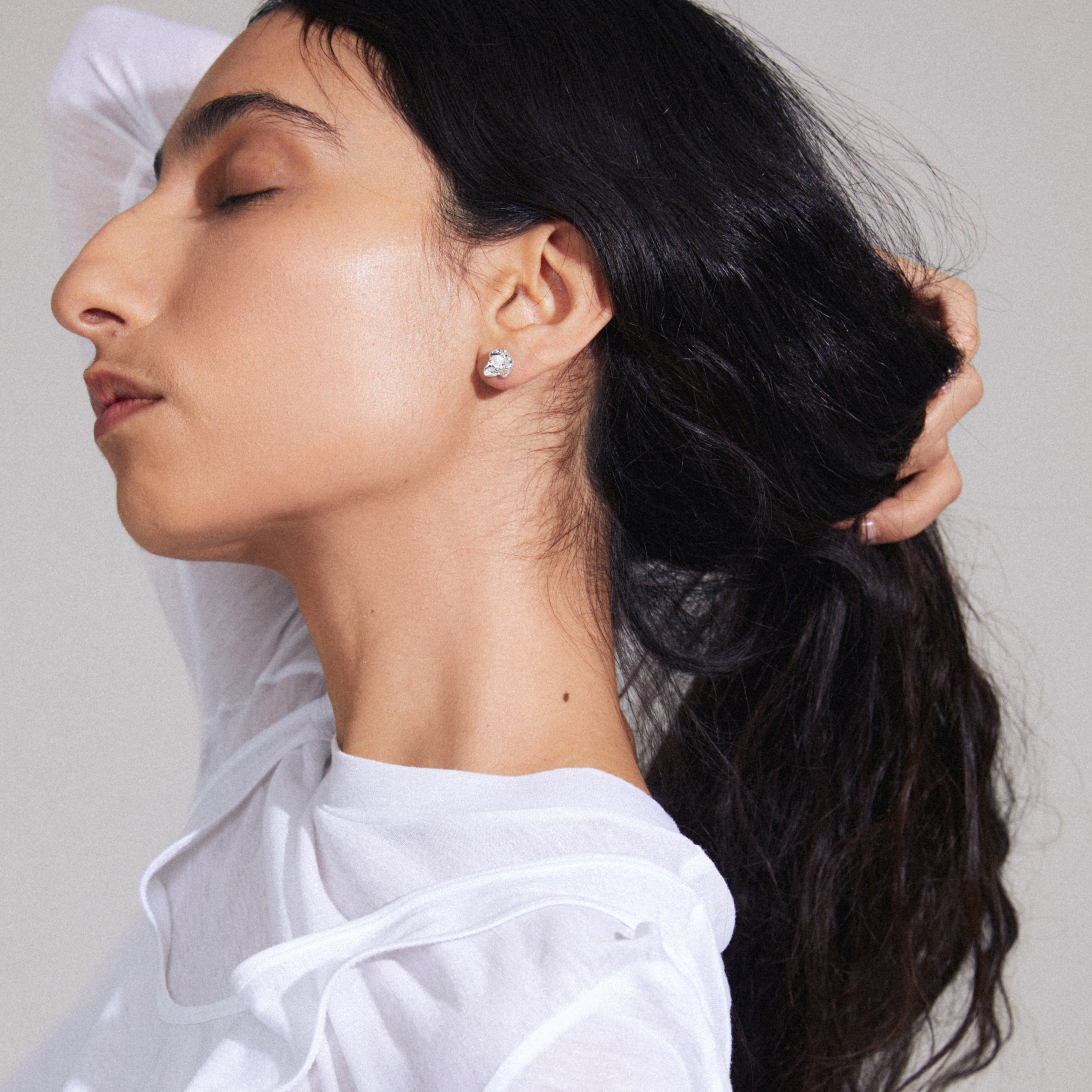 INAYA earrings silver-plated, featuring abstract seashell studs with central white glass beads, worn by a woman with a ponytail.