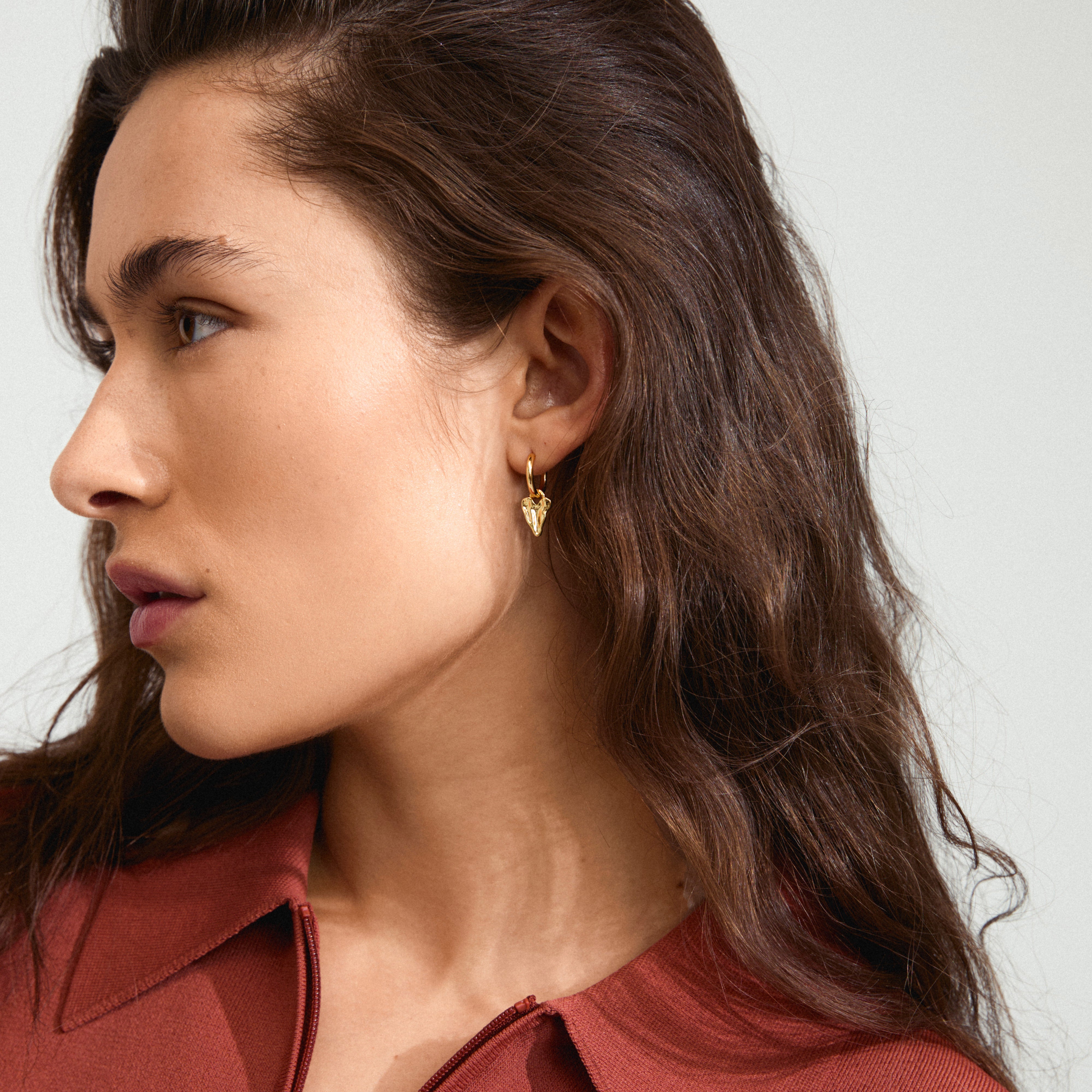 JULES gold-plated earrings featuring a small heart pendant, worn by a woman with long brown hair, showcasing their versatile, trendy design.