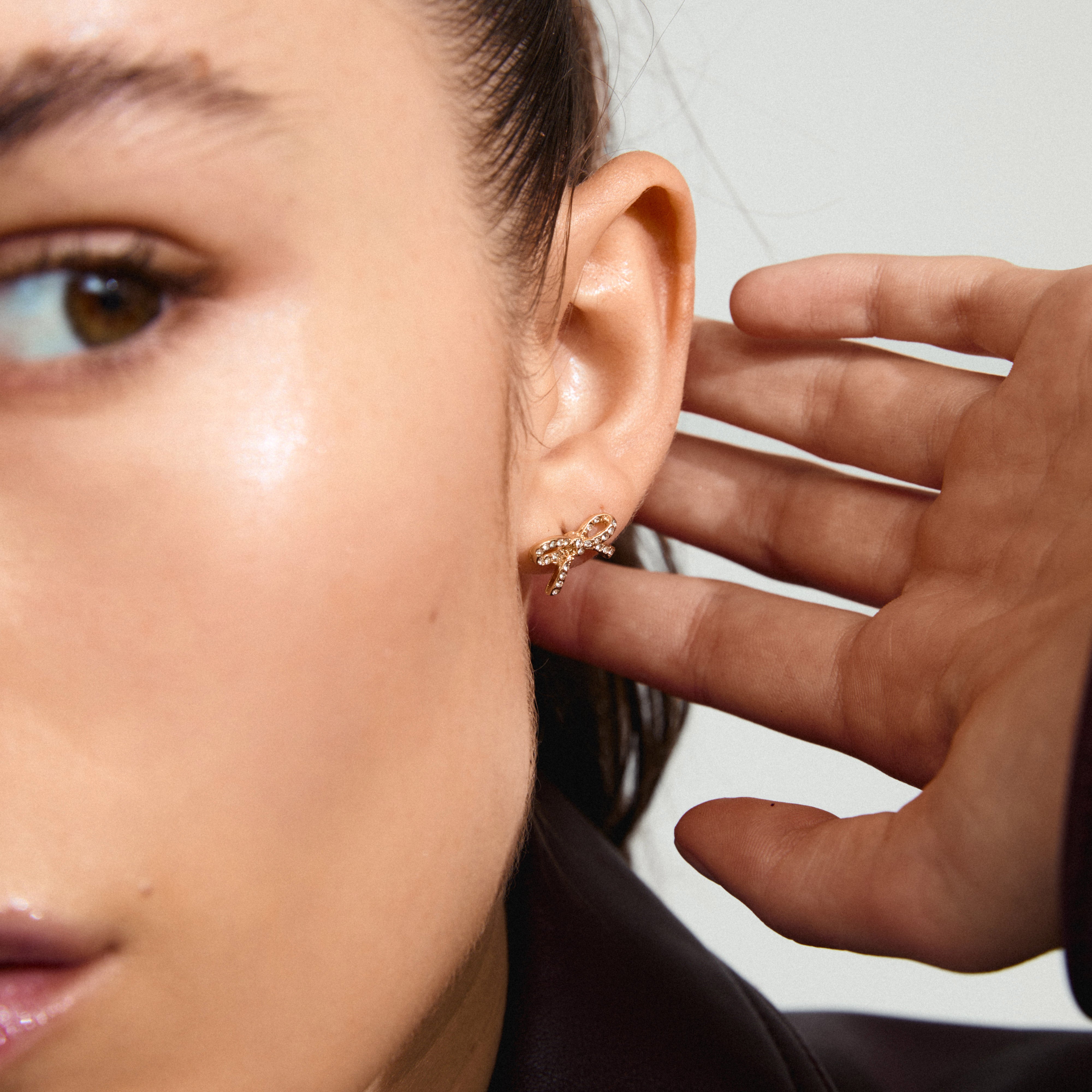 Close-up of a woman's ear wearing CATHARINA gold-plated bow earrings with sparkling Preciosa crystals, showcasing trendy and sustainable Danish design.