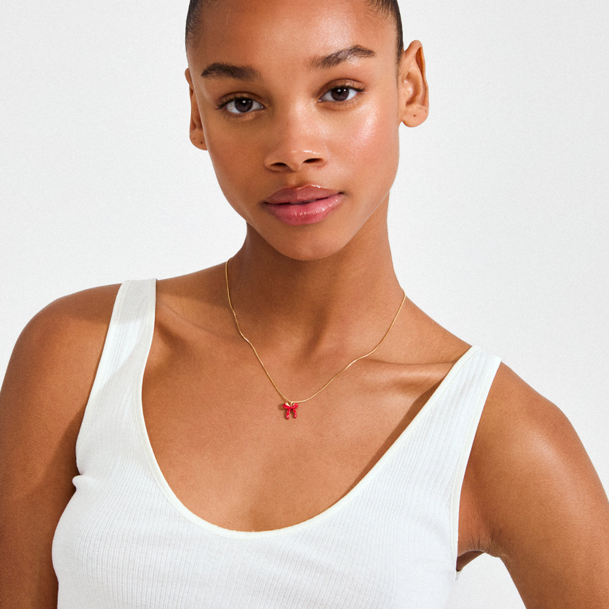 Young woman wearing the SIGRUN gold-plated necklace by Pilgrim, featuring a small red enamel bow charm on a delicate chain, exuding playful elegance.