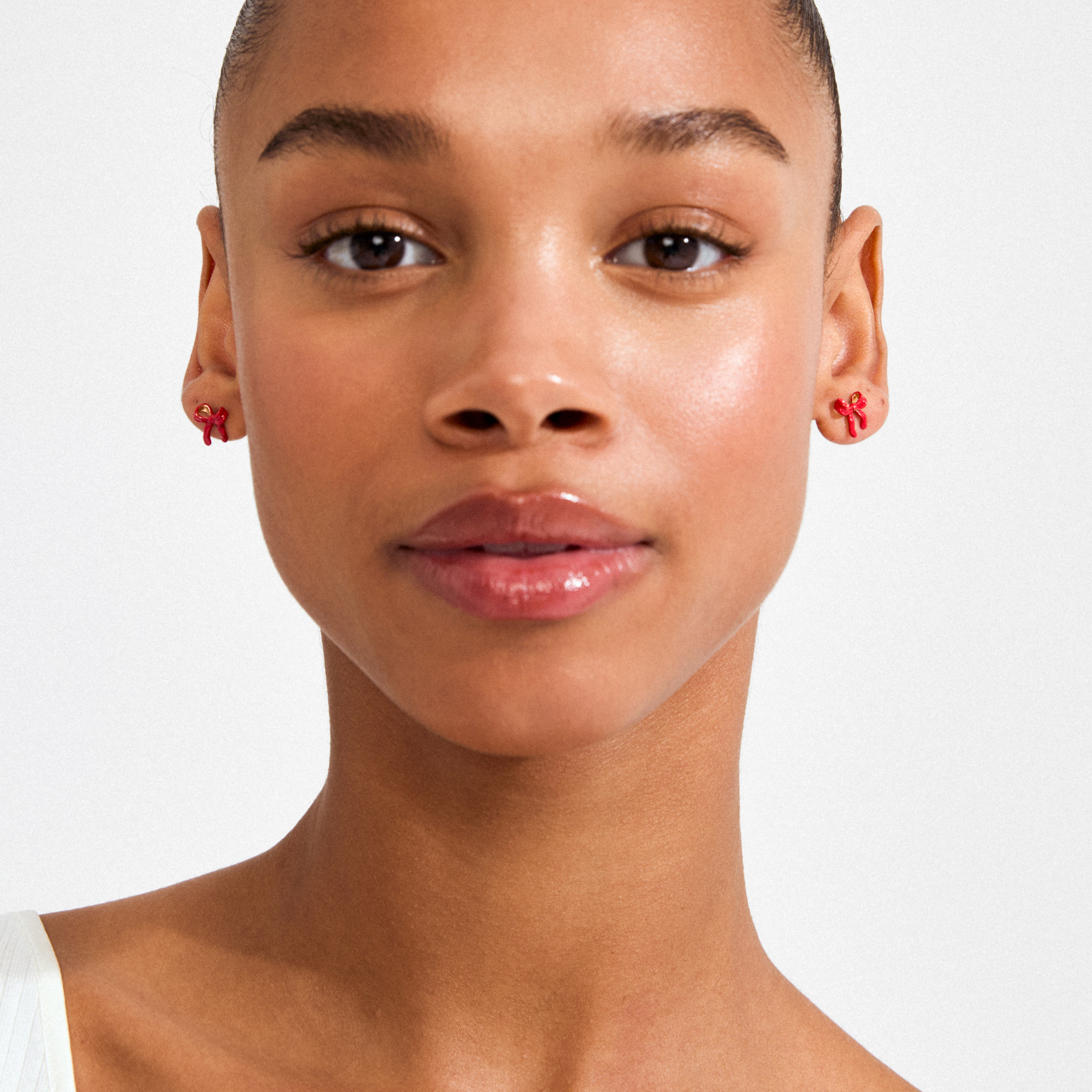 Young woman wearing SIGRUN earrings gold-plated, featuring small red enamel bow studs, showcasing Pilgrim's trendsetting, playful design with a minimalist touch.