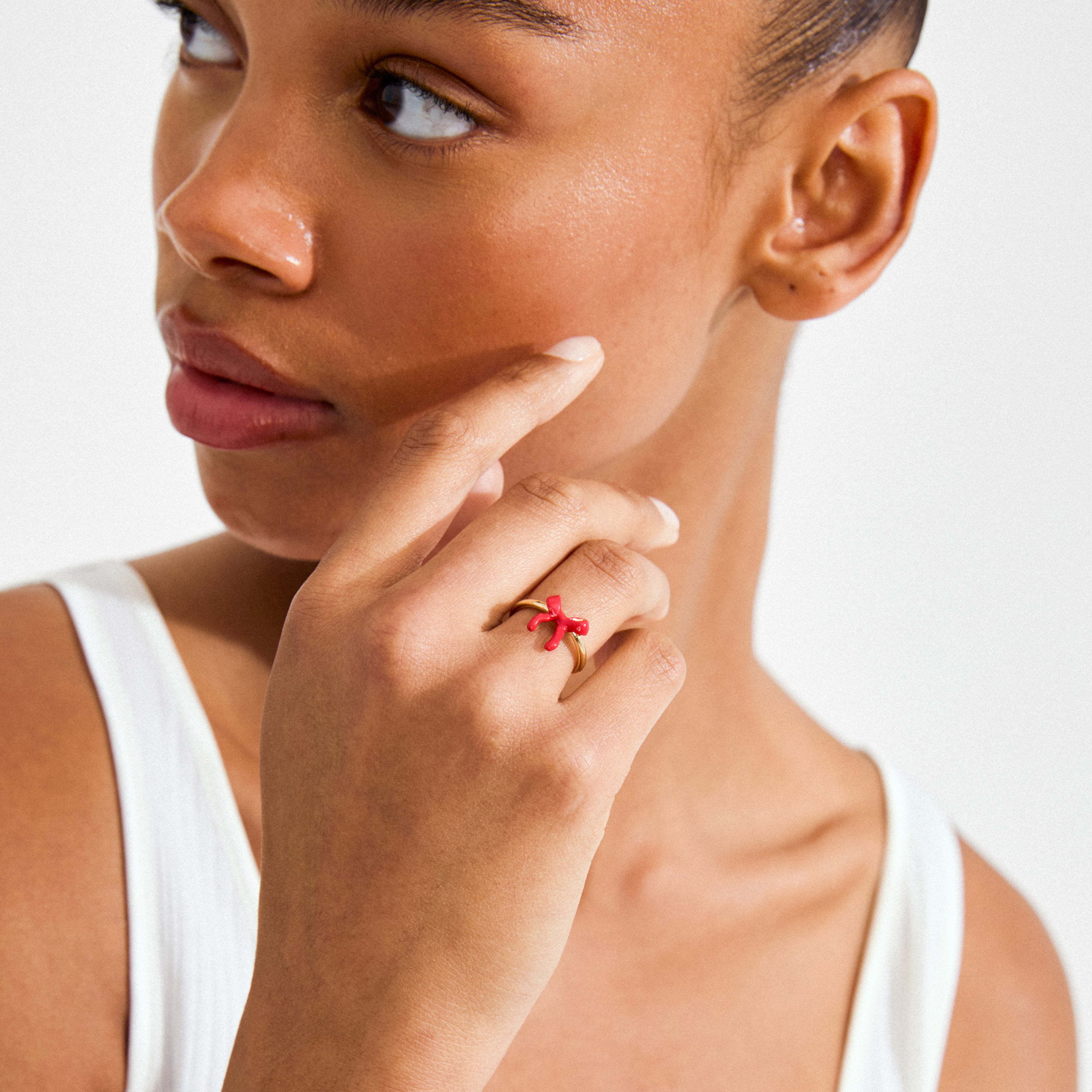 Woman wearing a white tank top displays the SIGRUN ring gold-plated by Pilgrim, featuring a chunky gold design with a red coral-shaped star.