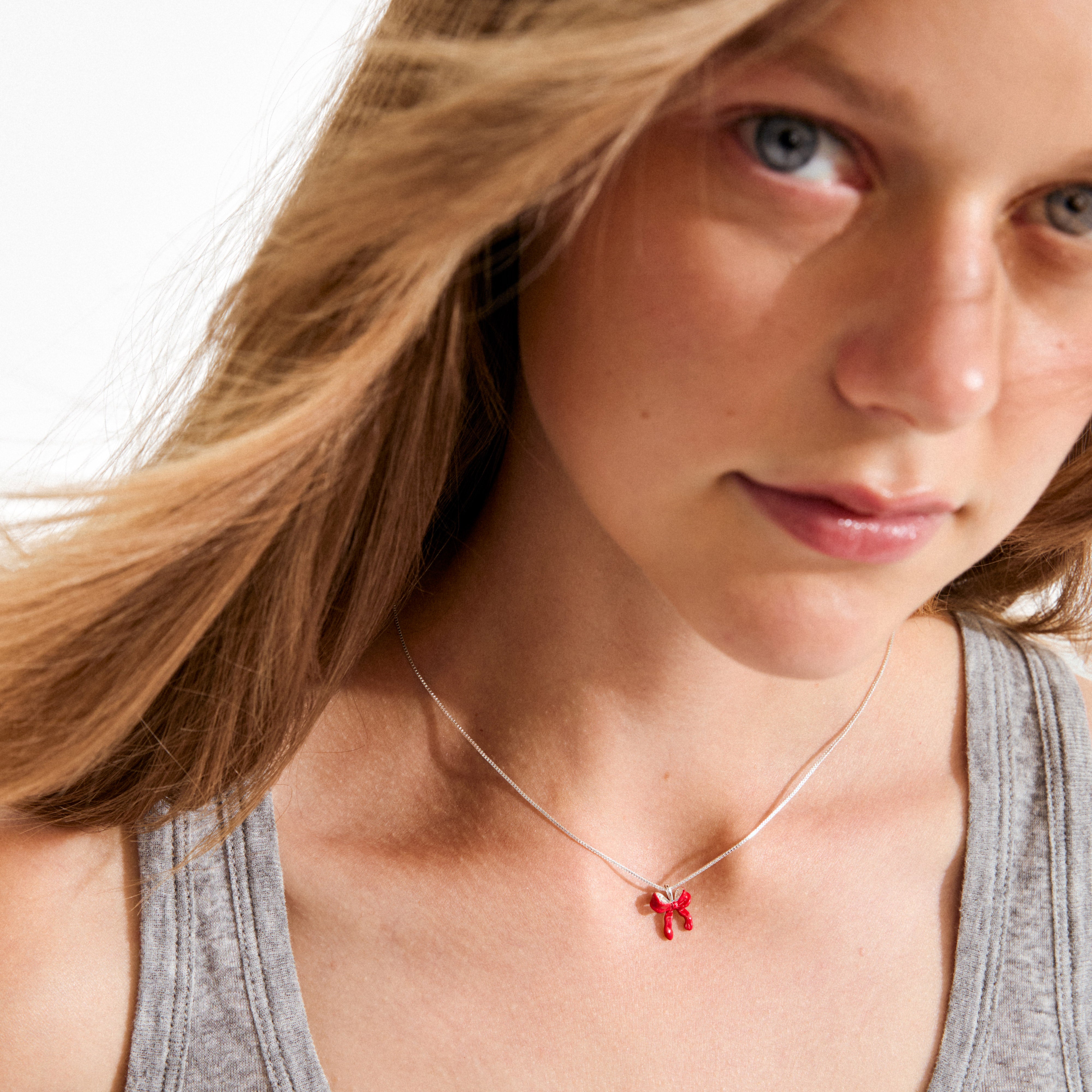 Young person wearing a light gray tank top, showcasing the SIGRUN necklace by Pilgrim, featuring a silver chain with a red balloon-animal dog pendant.