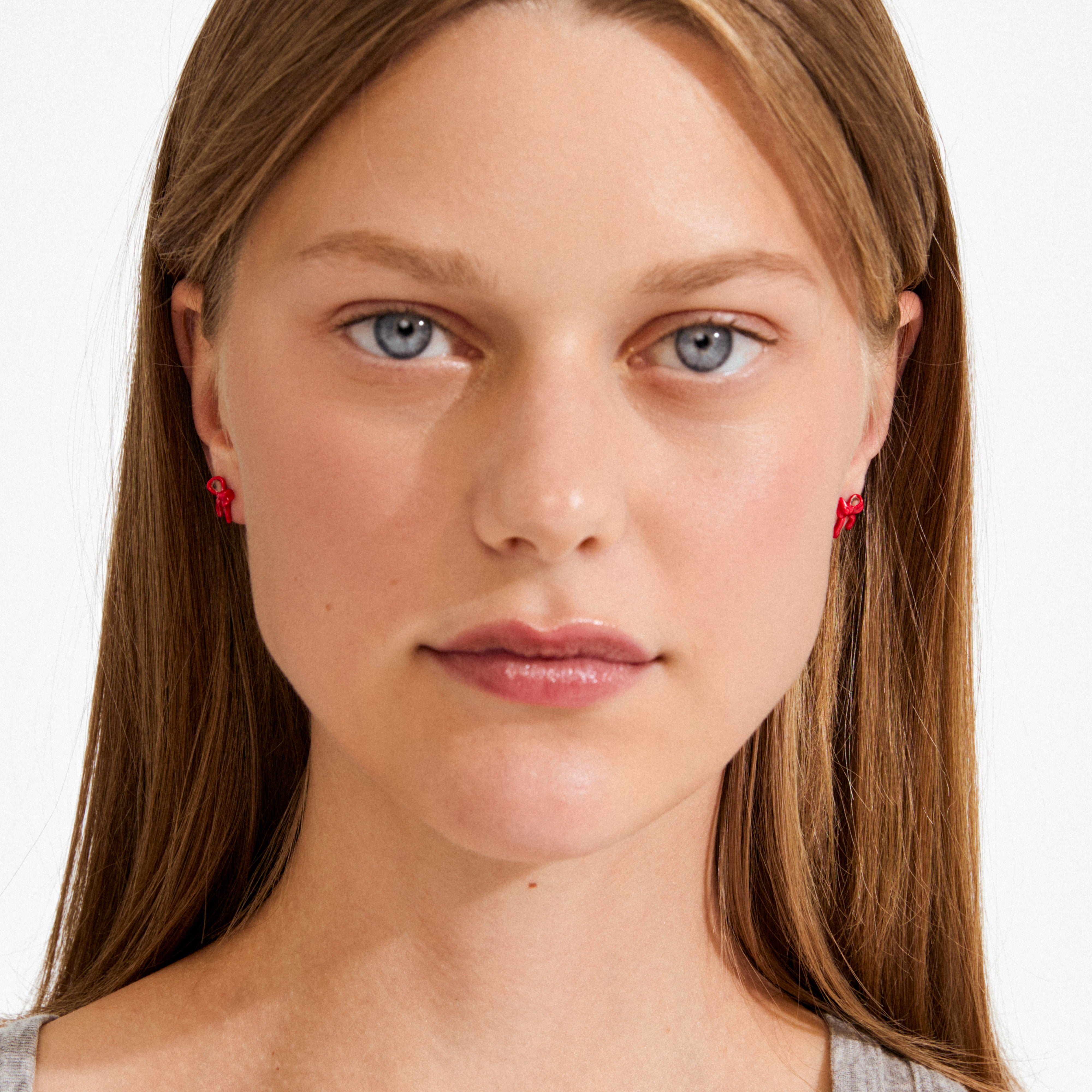 Young woman wears SIGRUN earrings, silver-plated red enamel bows, adding a trendy touch to her style. Perfect for minimalist or preppy fashion.