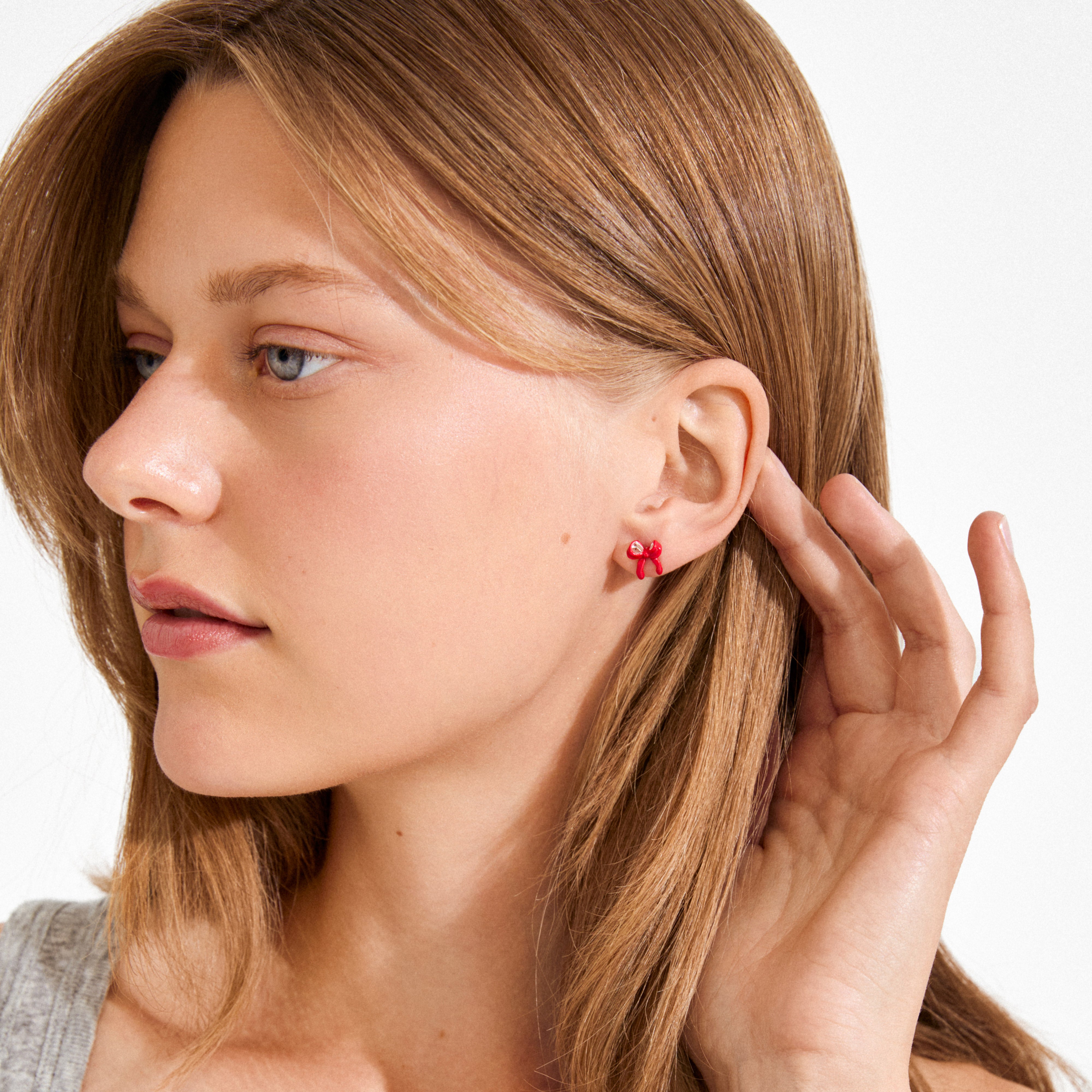 Young woman wearing SIGRUN earrings, featuring silver-plated red enamel bows, a playful accessory by Pilgrim, emphasizing minimalist or preppy styles with a sustainable touch.