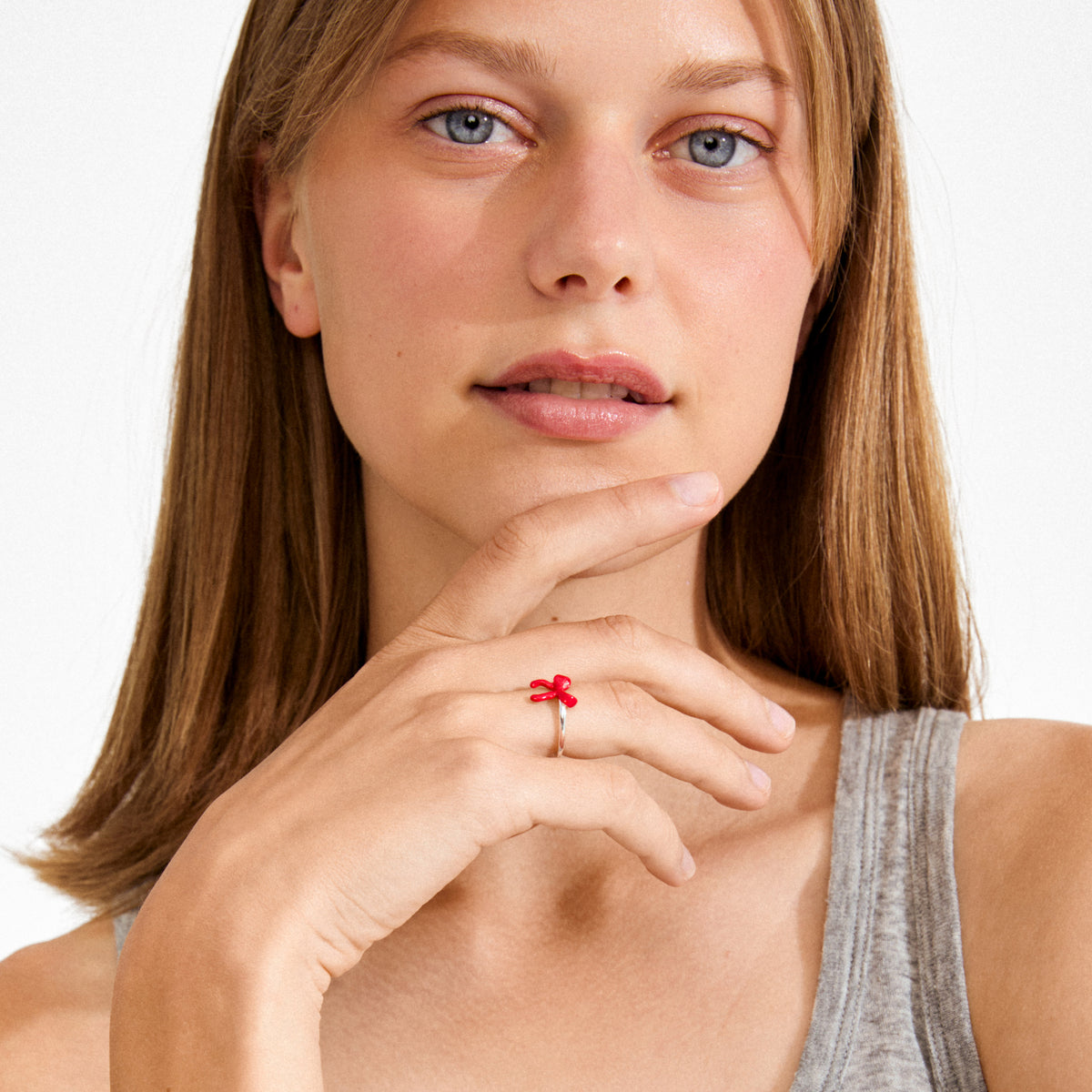 Young woman wearing SIGRUN ring silver-plated with red bow ornament on ring finger, highlighting its playful design and adjustable fit.